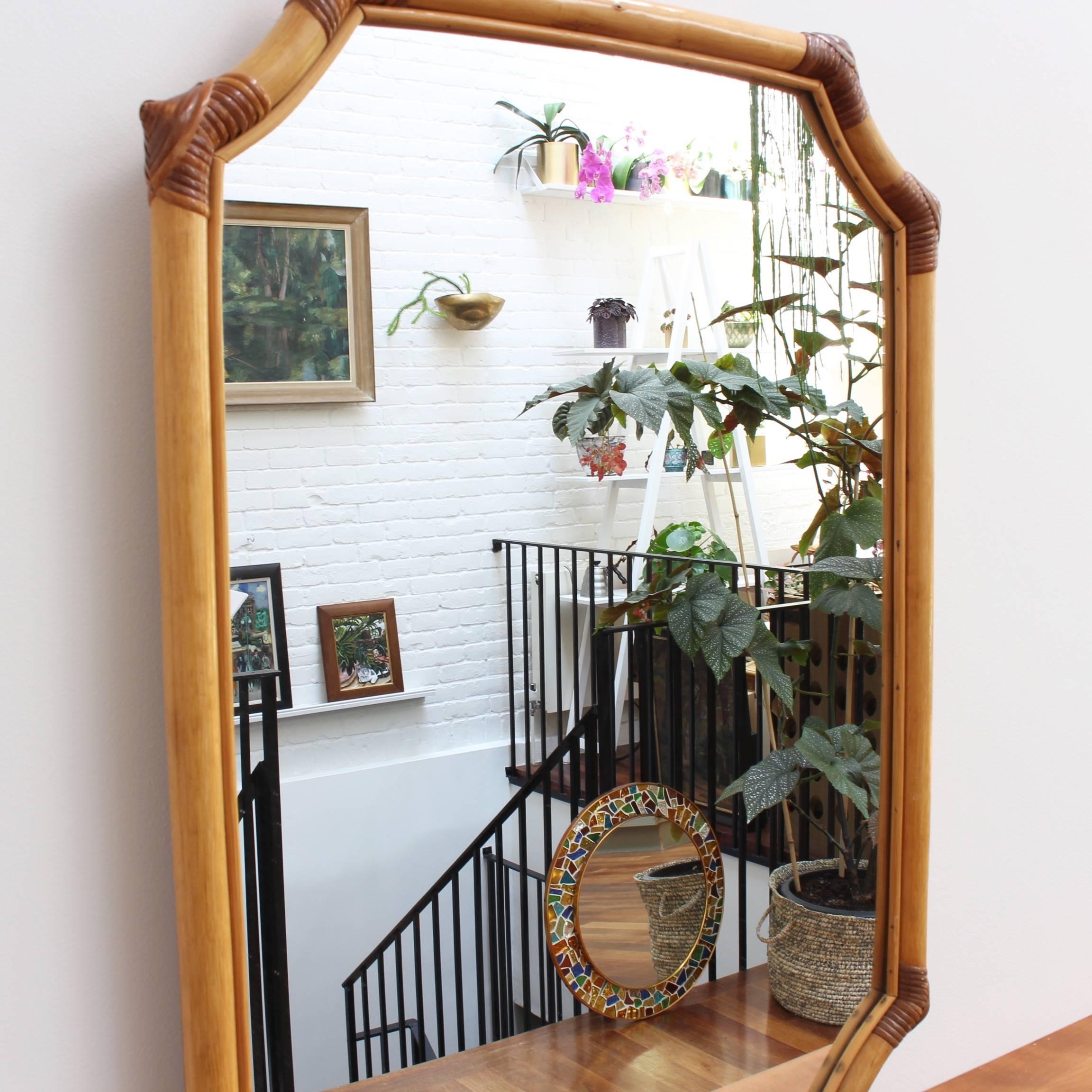 French bamboo and rattan vintage wall mirror, circa 1960s. This mirror has a delightful Asian-inspired shape formed by the bamboo frame and held together with rattan ties on the edges and curves. There is a characterful, aged patina and some