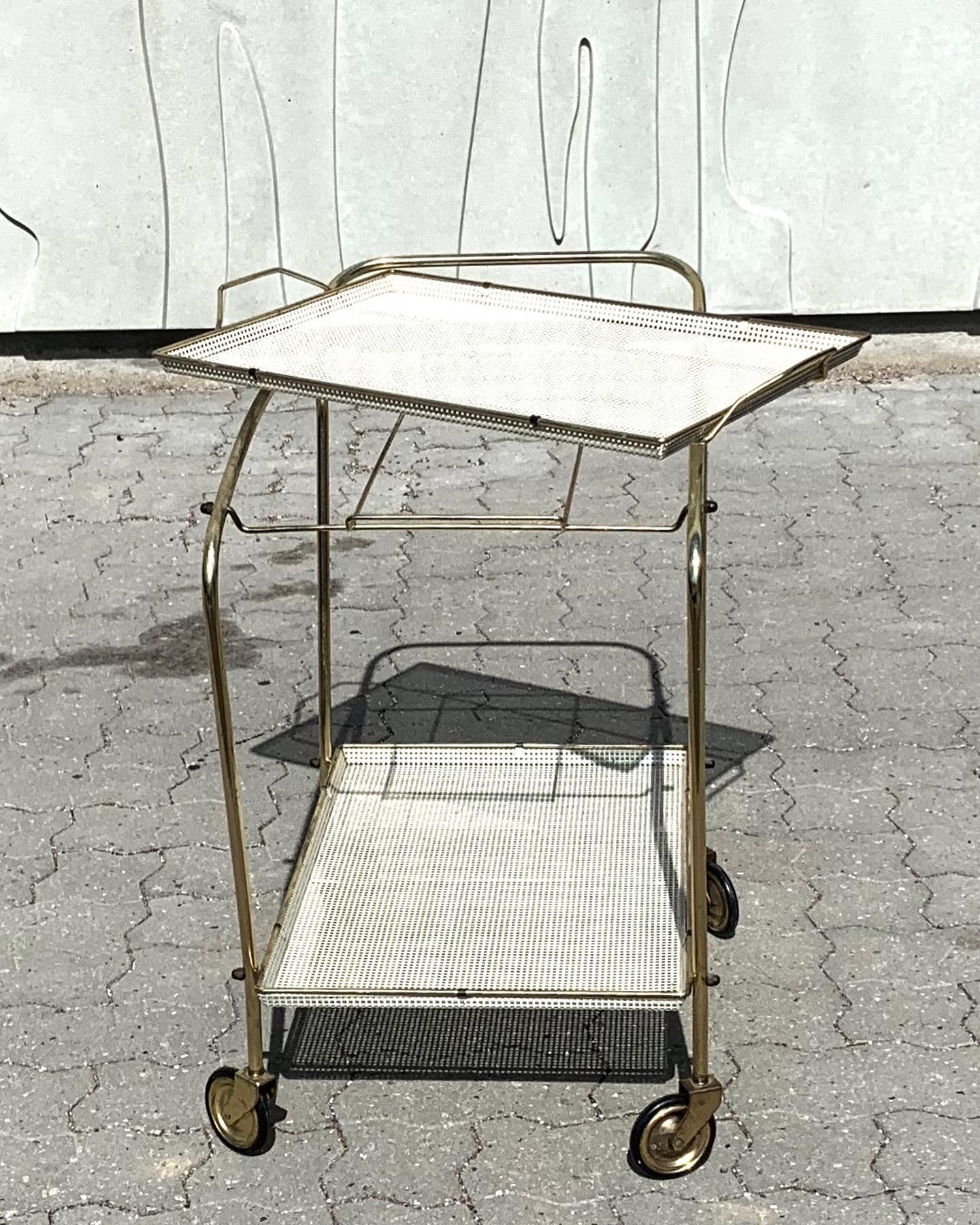 This bar cart in the style of Mathieu Matégot, circa 1950 consists of wire steel and brass, perforated white coated sheet metal and four wheels made of brass.
The top tray is removable and so very practical to serve your drinks or beverages.
 