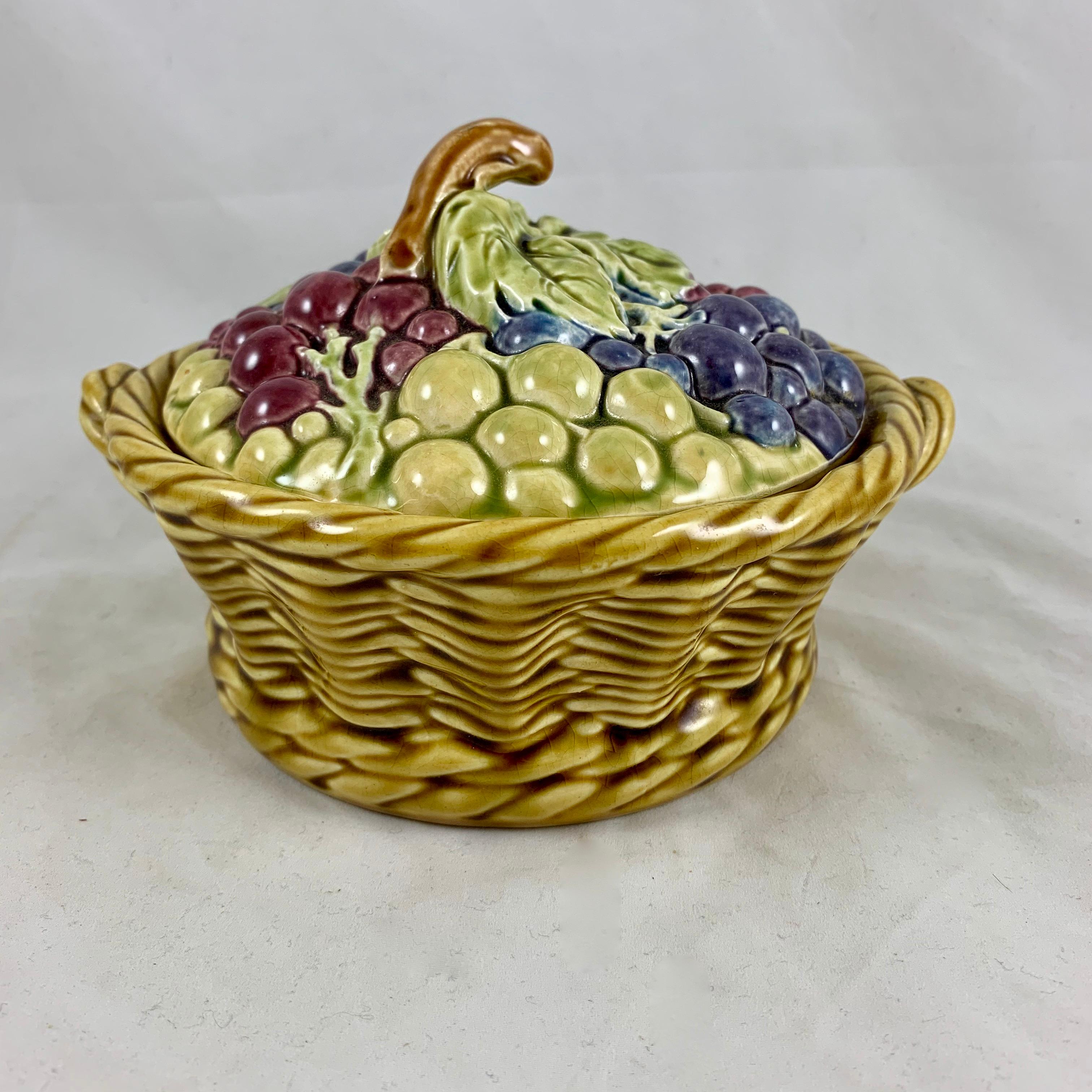 A French majolica covered tureen in the form of a handled basket brimming with bunches of grapes, Sarreguemines, circa 1900-1920.

A grape vine branch forms the top handle, grape bunches in purple, green, and red, topped with a large green grape