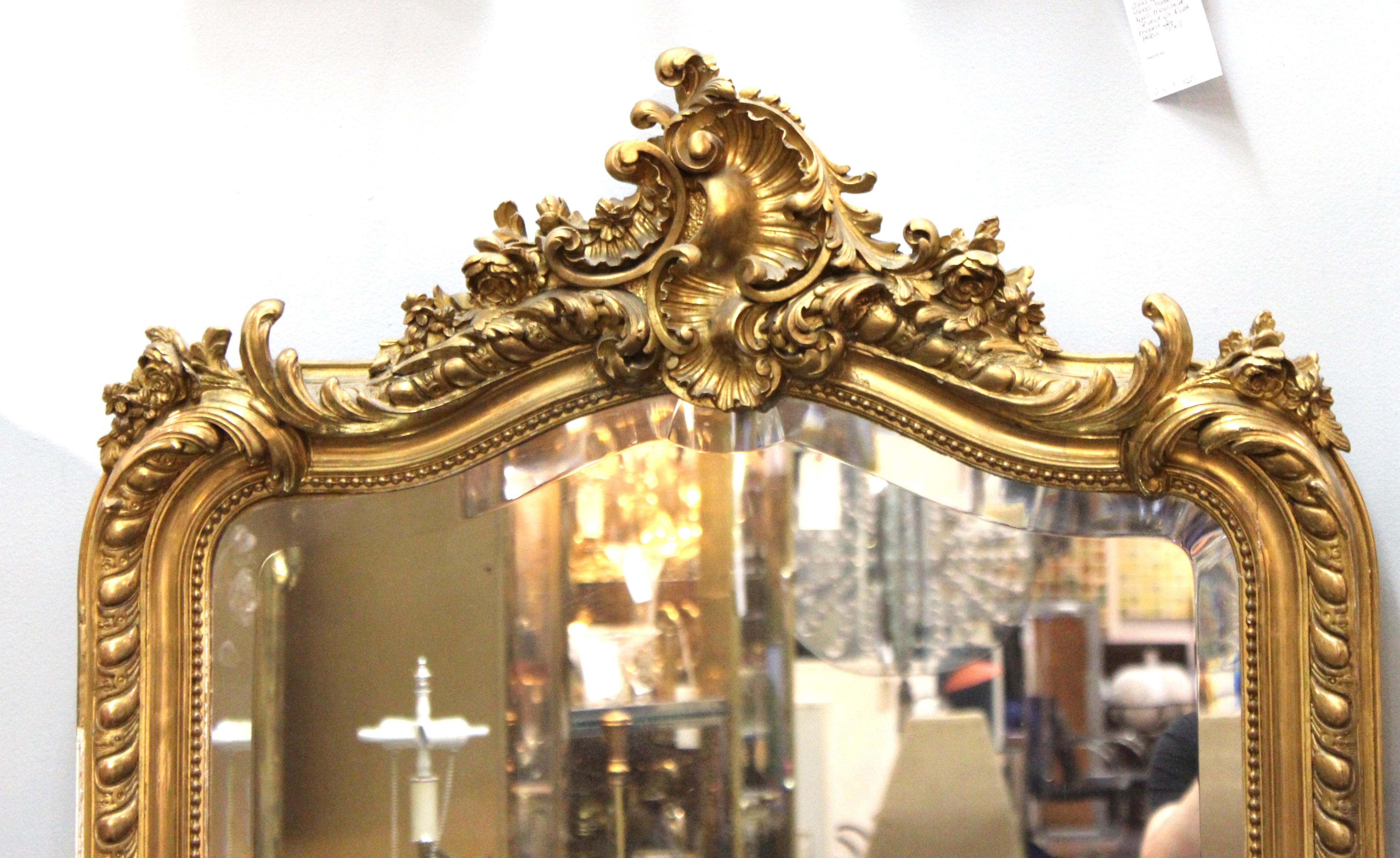 French Baroque Revival wall mirror with carved and gilt wooden frame with decorative swags, leaves and floral elements. The piece was made in France in the late 19th century. In great antique condition with age-appropriate wear and some old