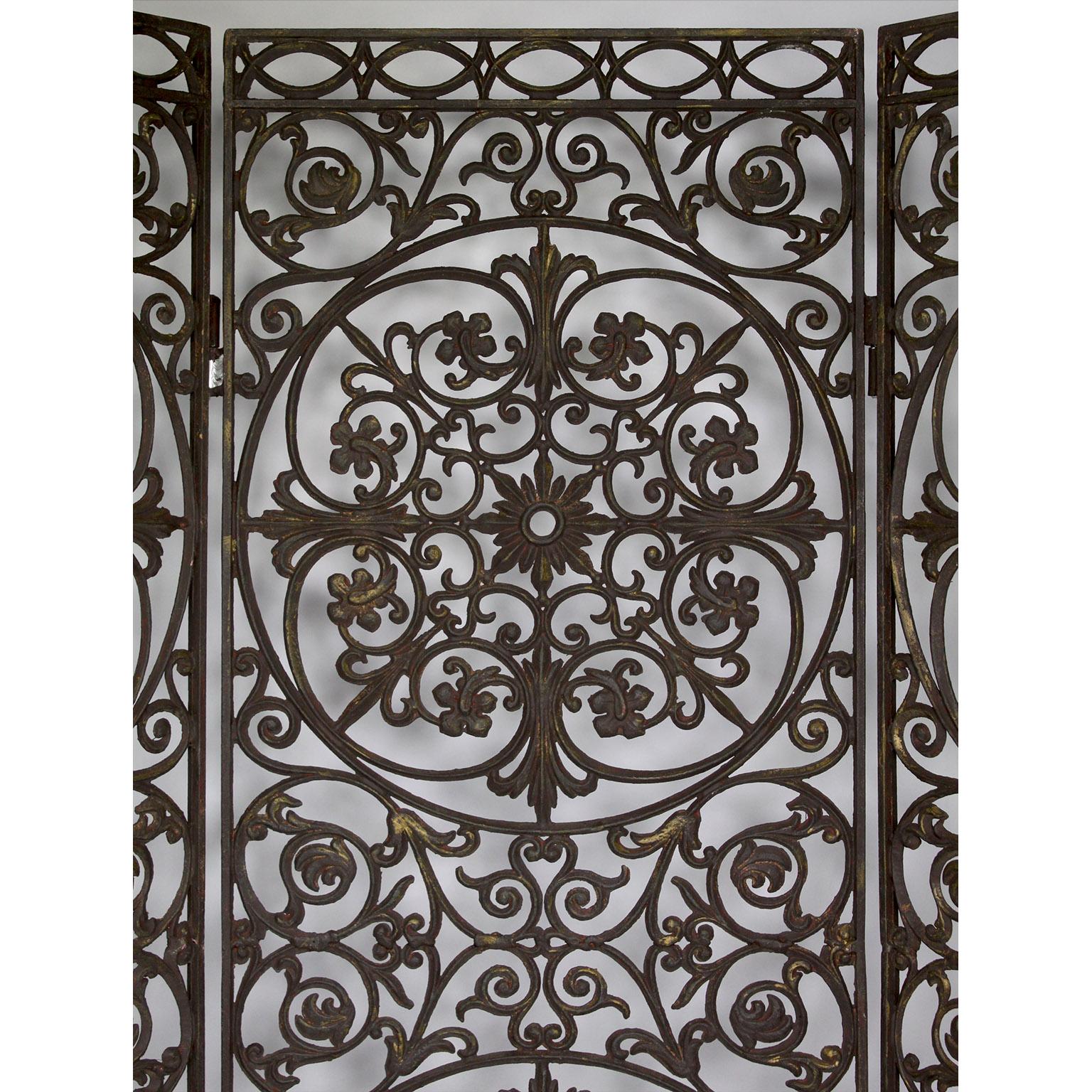 Séparateur d'écran autoportant à trois panneaux en métal percé et doré, de style néo-baroque français. Écran en fer forgé orné d'un motif floral et de volutes dans des cadres circulaires, avec des rayons de soleil et des rosettes. Circa : 20ème