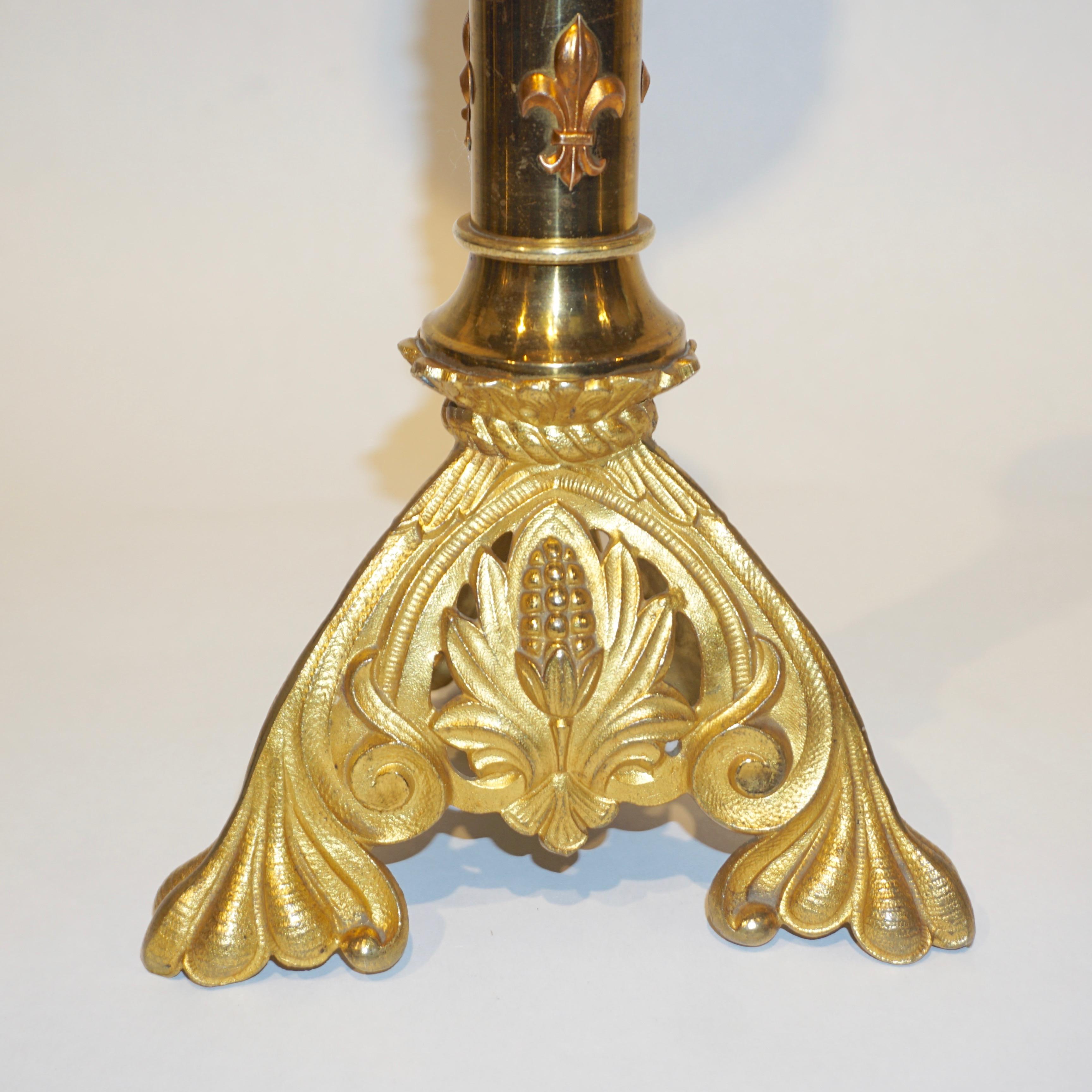 French handcrafted gold color candle holders in gilt bronze with high quality decoration, the tallest decorated with copper fleur-de-lis in relief, each with a Baroque Revival bronze base elegantly decorated with open fretwork and fitted with a tall