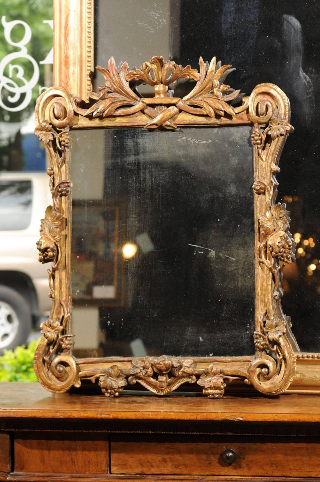 A French Baroque style giltwood mirror, carved with grapes, vines and volutes from the 19th century. This French medium size wall mirror features an exquisite Baroque style frame, adorned with delicate volutes accentuating each of the four corners,