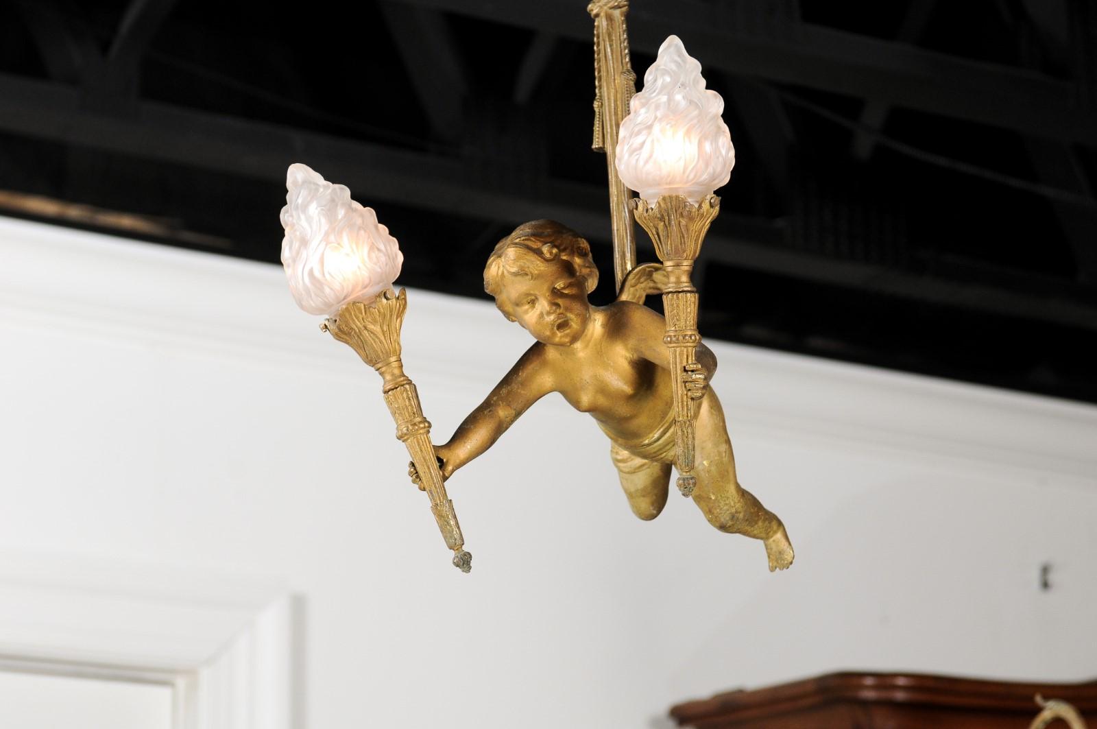 A French Baroque style gilt bronze two-light chandelier from the 19th century, depicting a cherub holding two torches. Born in France during the 19th century, this bronze doré (gilt bronze) chandelier features a long central bronze tassel from which