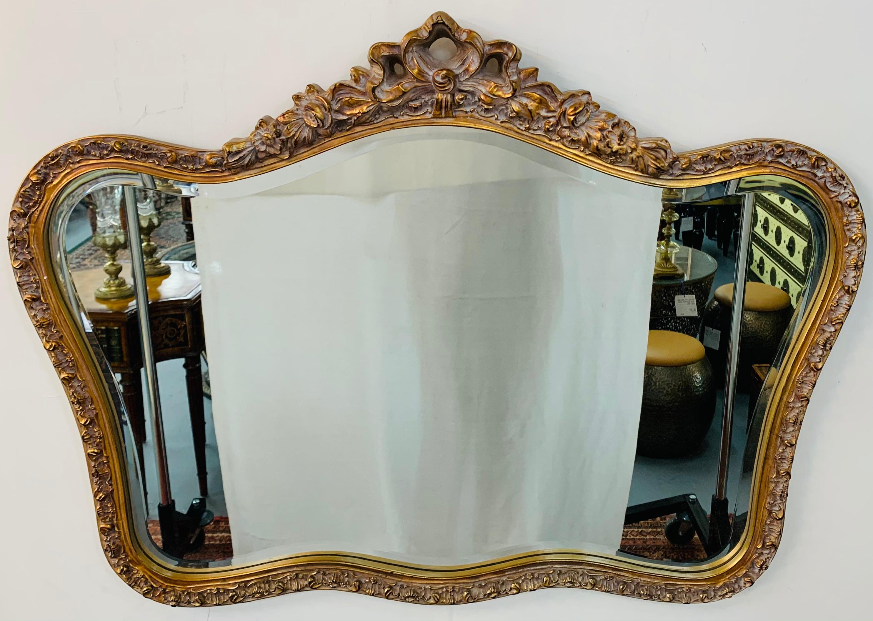 A beautiful French giltwood mirror. The mirror is finely carved with amazing details and features a charming bow / ribbon with flowers and a beveled edge glass mirror. This mirror displays horizontally and can be placed in multiple areas such as