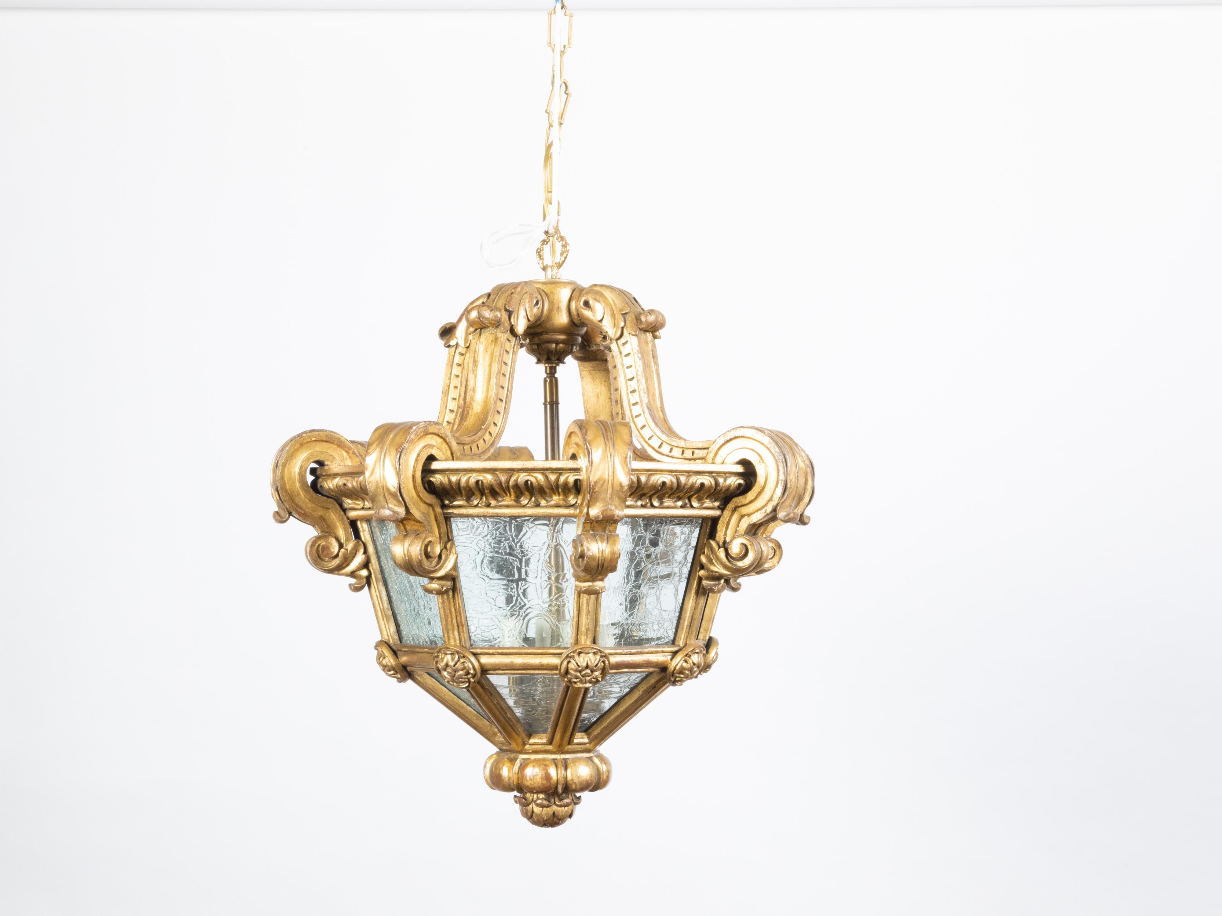 A French Baroque style giltwood lantern from the early 20th century, with volutes and textured glass. Created in France at the Turn of the Century, this lantern captures our attention with its golden tones and scrolling lines. Delicate volutes