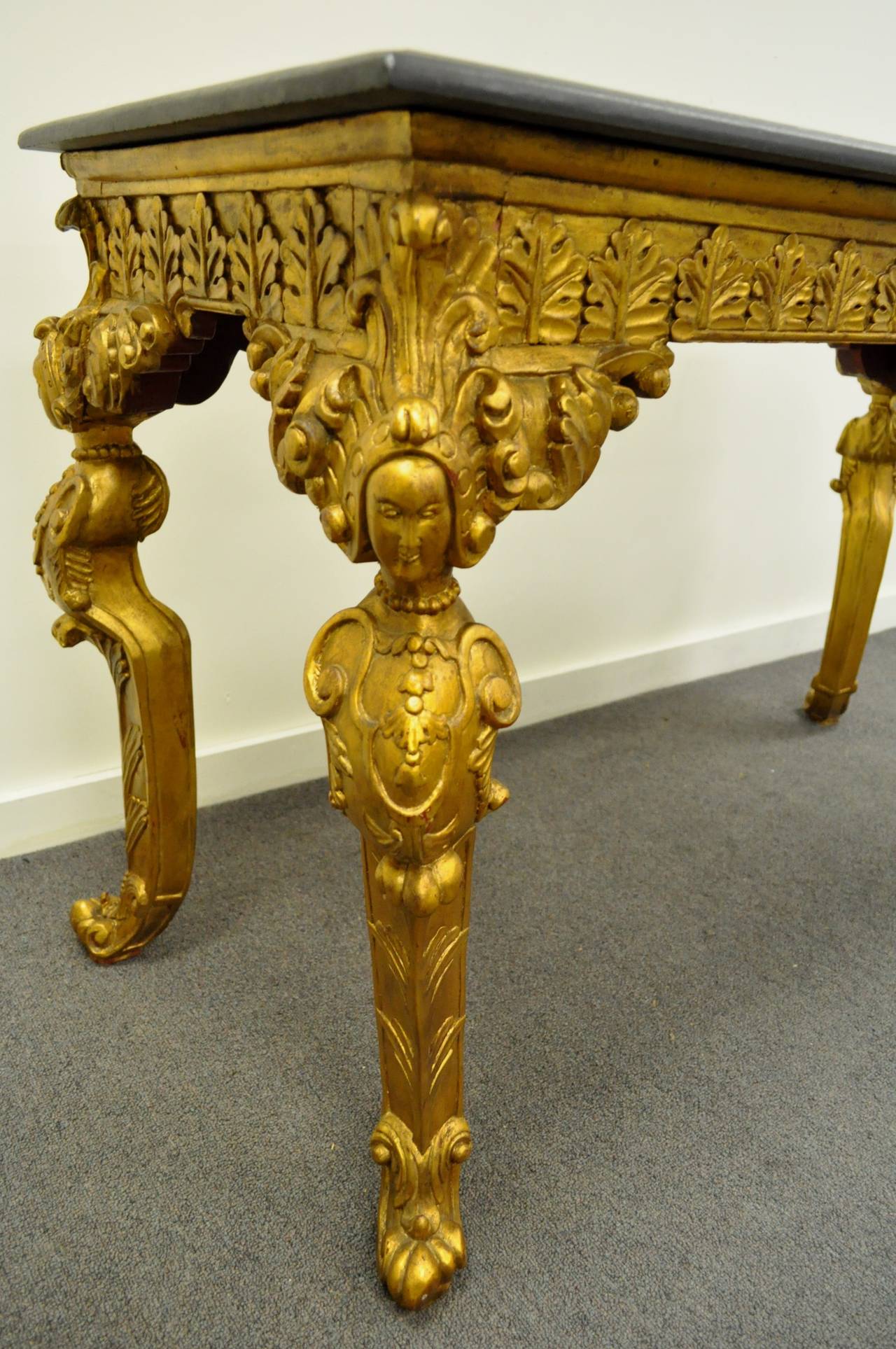 Striking vintage French Baroque style gold gilt carved wood and marble top console table. The table features shapely cabriole legs with elaborately carved female figures, acanthus accents around the skirt, and a thick marble top.