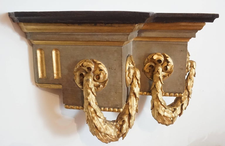 A large last half of the 19th century French Baroque style stained, painted, and parcel-gilt wall bracket of unusual bisected cornice form having stained chestnut shelf above compound-moulding surmounting flat frieze with exquisitely carved rosette