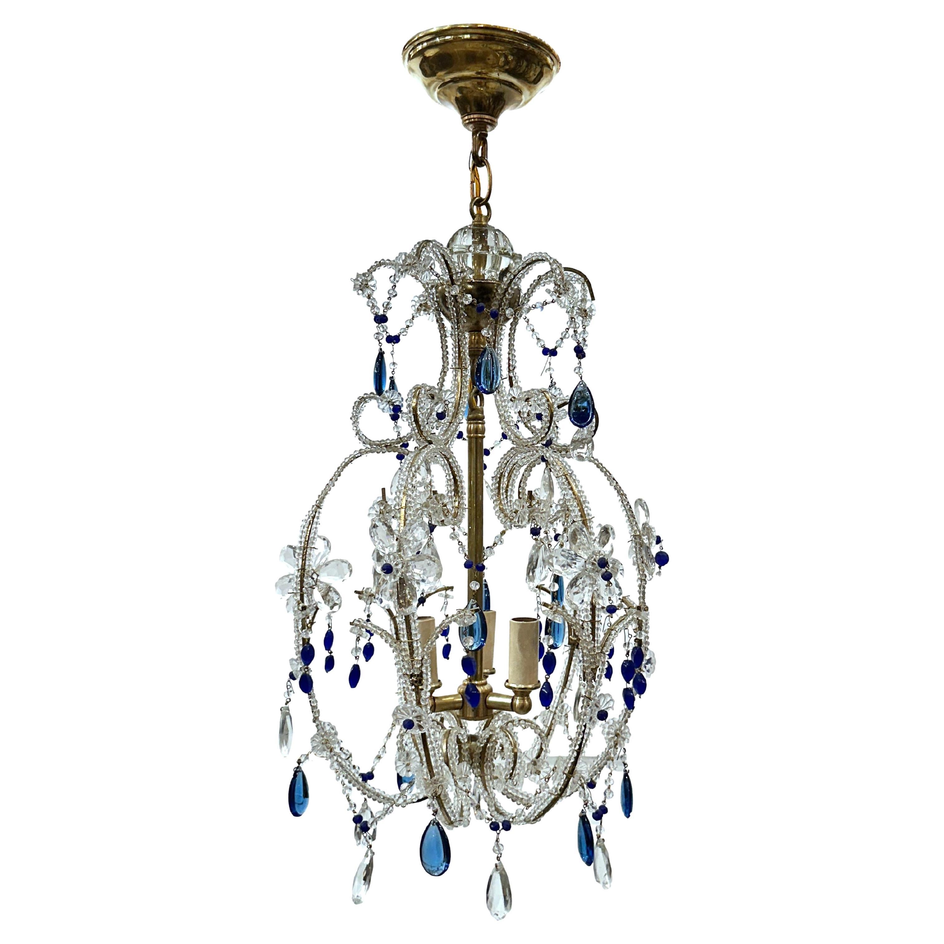 A circa 1950’s beaded gilt metal chandelier with blue glass drops and 3 interior lights.

Measurements:
Drop: 26″
Diameter: 12″