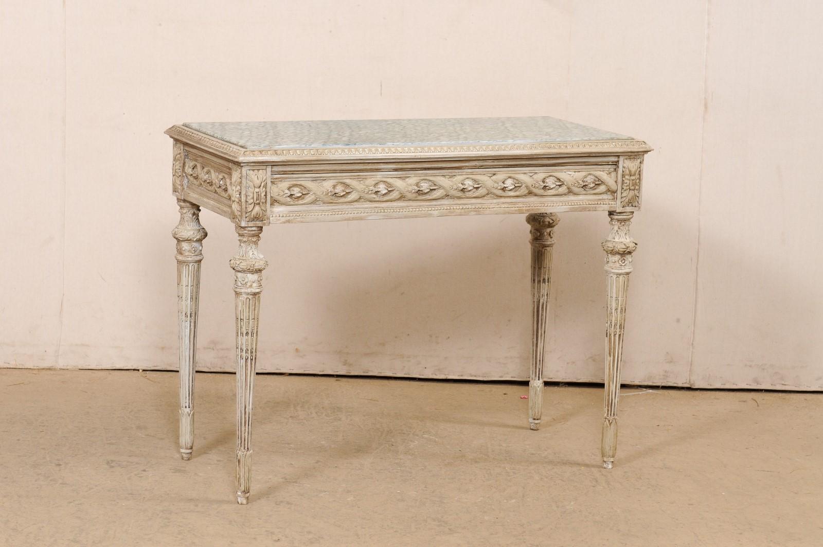A French carved-wood console table with drawer and marble top. This vintage table from France has a rectangular-shaped top with recessed marble framed within a lamb's tongue carved edging. The apron, which is magnificently carved in a floral