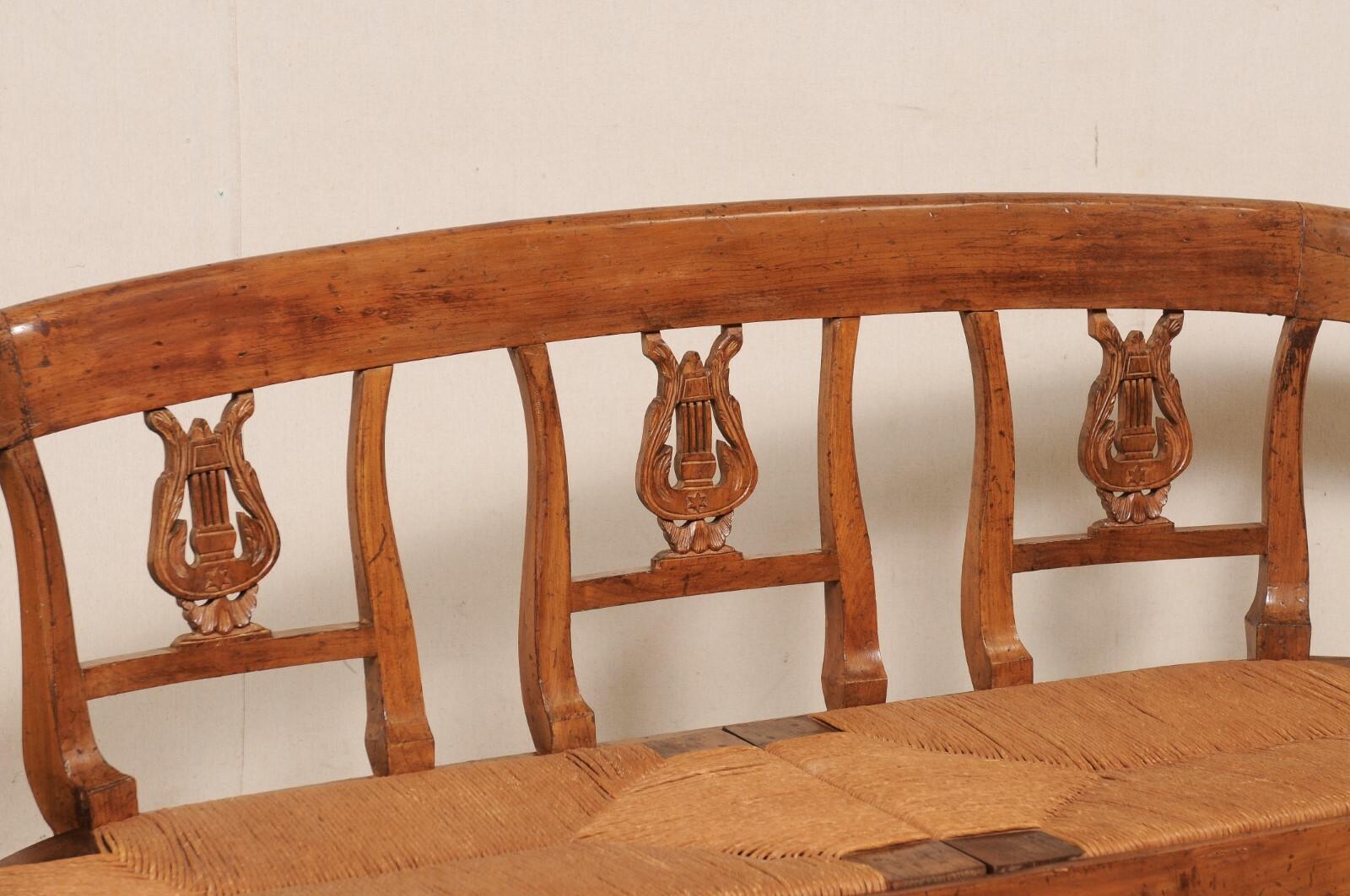 A French Neoclassic carved-wood sofa bench with rushed seat from the 19th century. This antique bench from France has been beautifully carved with Neoclassical details, featuring a gracefully curved top rail which gives way to an open back with