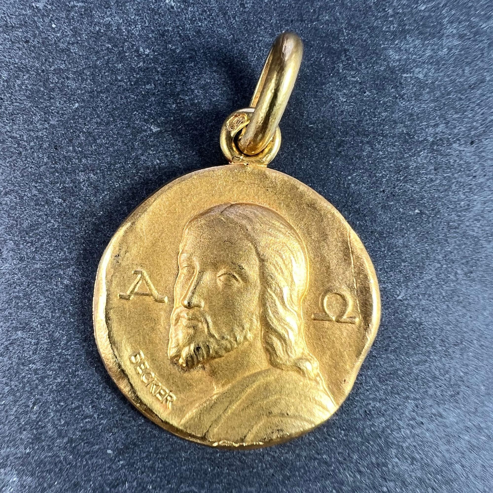 A French 18 karat (18K) yellow gold charm pendant designed as a round medal depicting Jesus Christ with the symbols for Alpha and Omega to either side. Signed Becker, stamped with the eagle’s head for 18 karat gold and French manufacture, along with