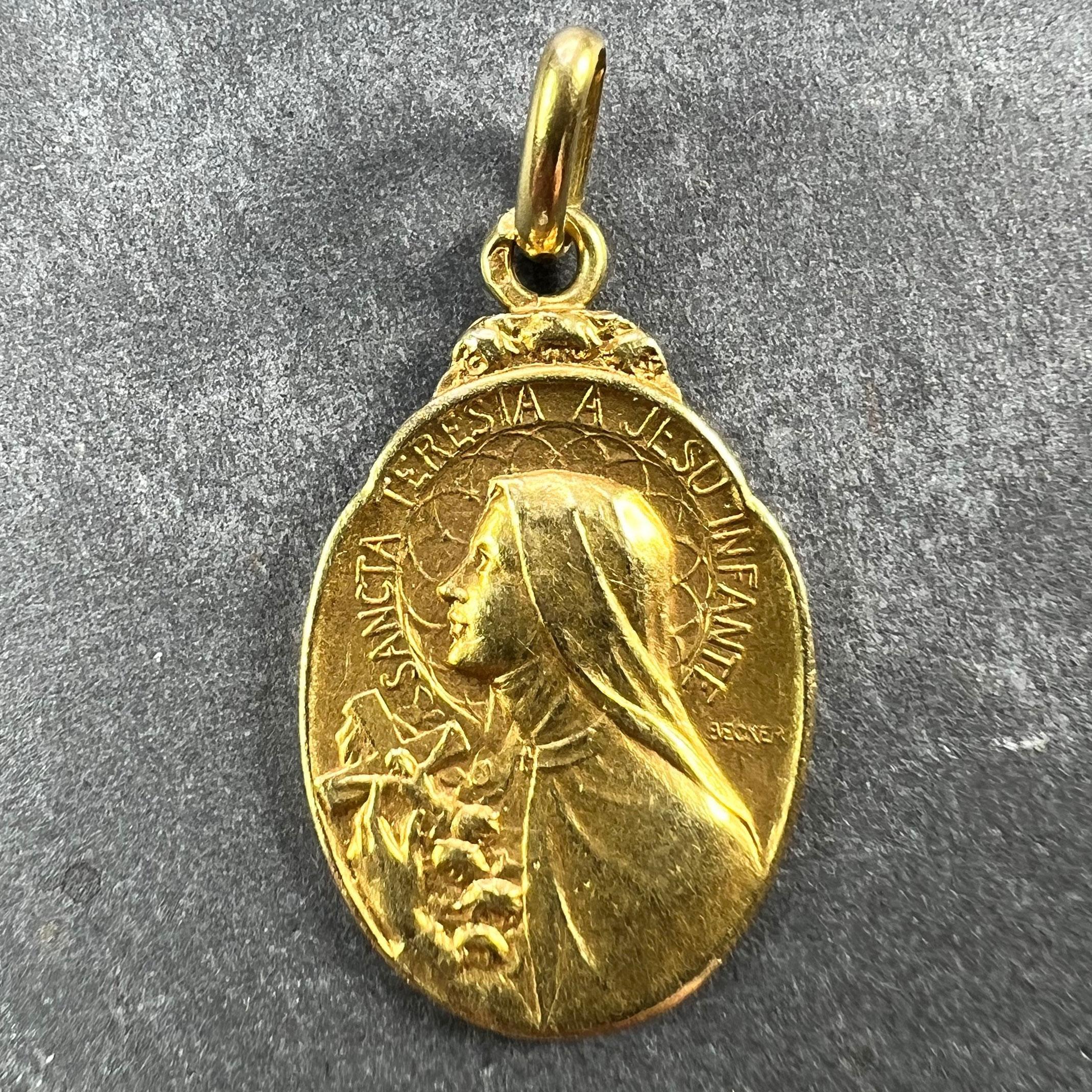 A French 18 karat (18K) yellow gold charm pendant designed as an oval medal depicting Saint Therese with a halo with the phrase 'SANCTA THERESIA A JESU INFANTE' (Saint Therese of the Infant Jesus) holding a crucifix and some roses, the halo with