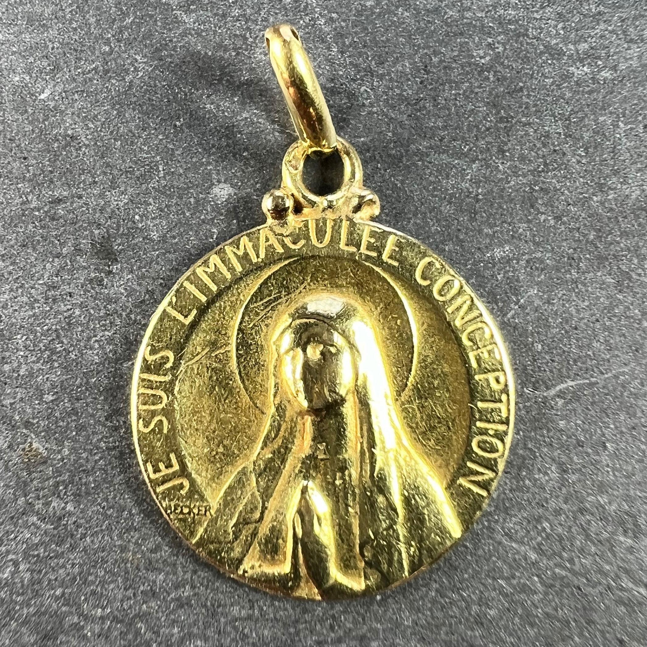 A French 18 karat (18K) yellow gold charm pendant depicting the Virgin Mary at prayer surrounded by the phrase 'JE SUIS L'IMMACULEE CONCEPTION'. The reverse depicts a relief of a wreath of roses. Signed Becker and stamped with the eagle mark for 18