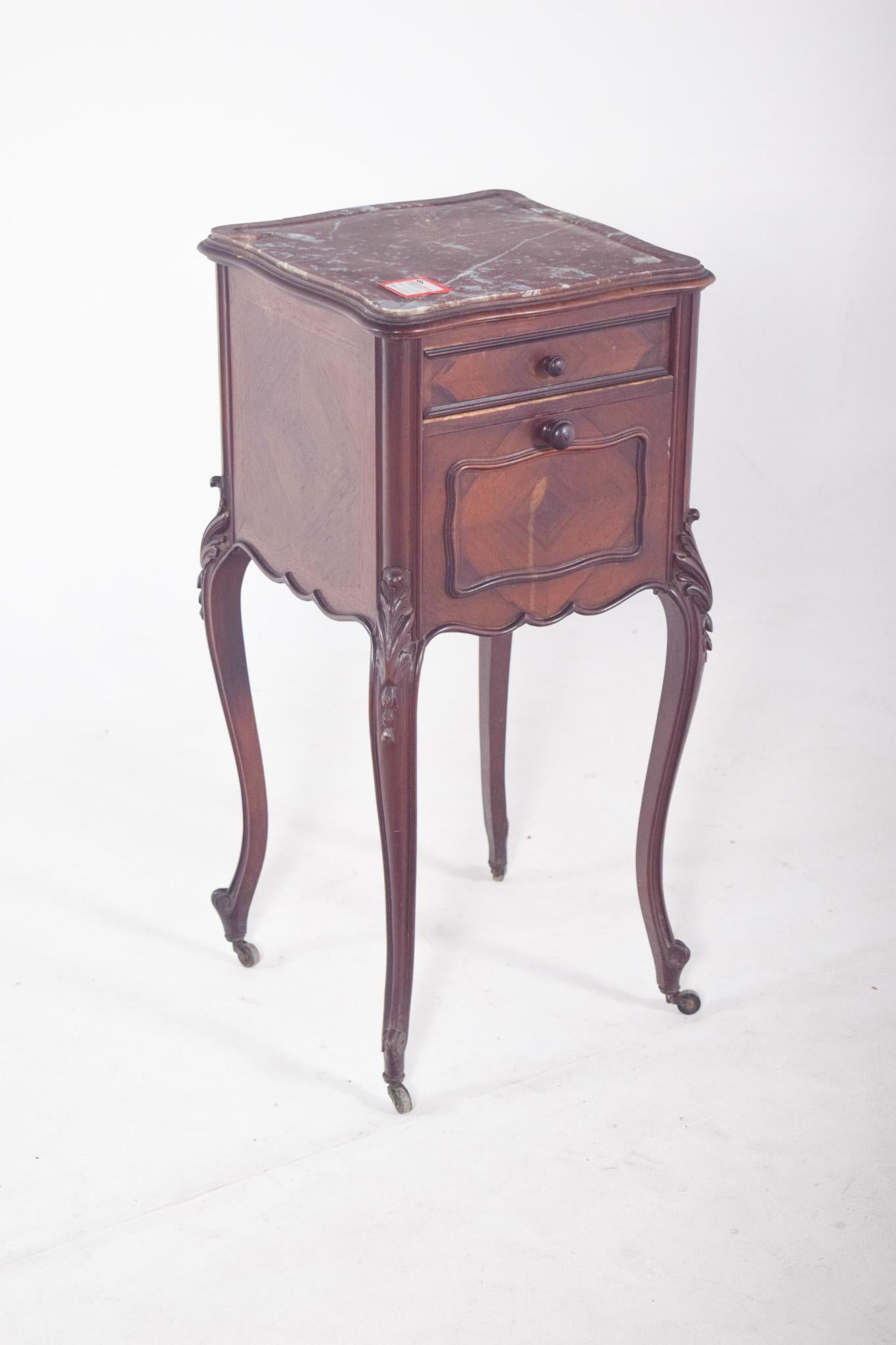Bedside table in rosewood with marble top. The structure is tall and narrow, supported by four curved legs with small wheels, which facilitates mobility. It has two drawers, a small one at the top and a larger one just below, both with round