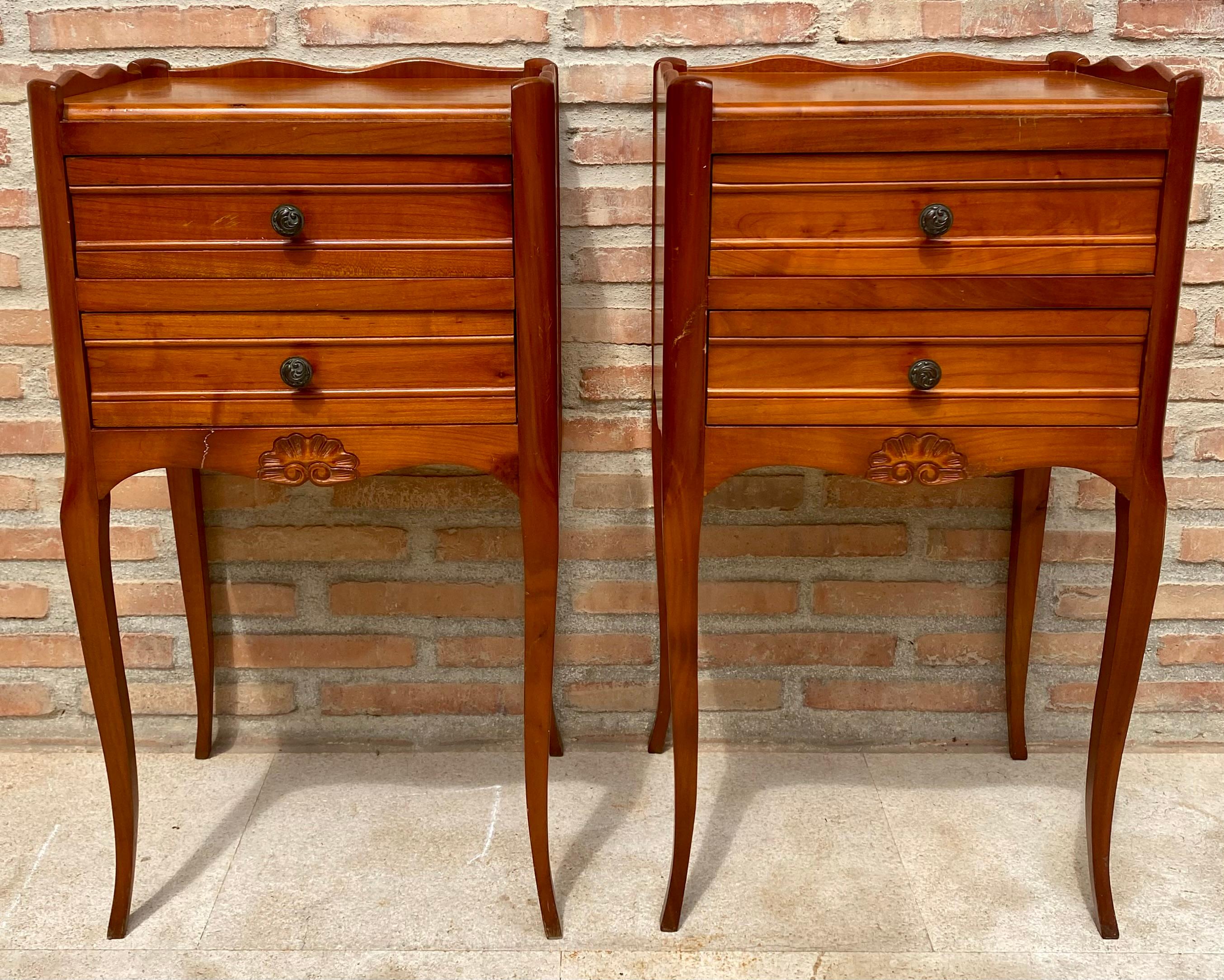 A fine pair of French bedside end tables or nightstands - each Stand featuring a scalloped edge gallery over a frieze of two drawers with brass pulls, apron bottom, and set upon four tapering cabriole legs.