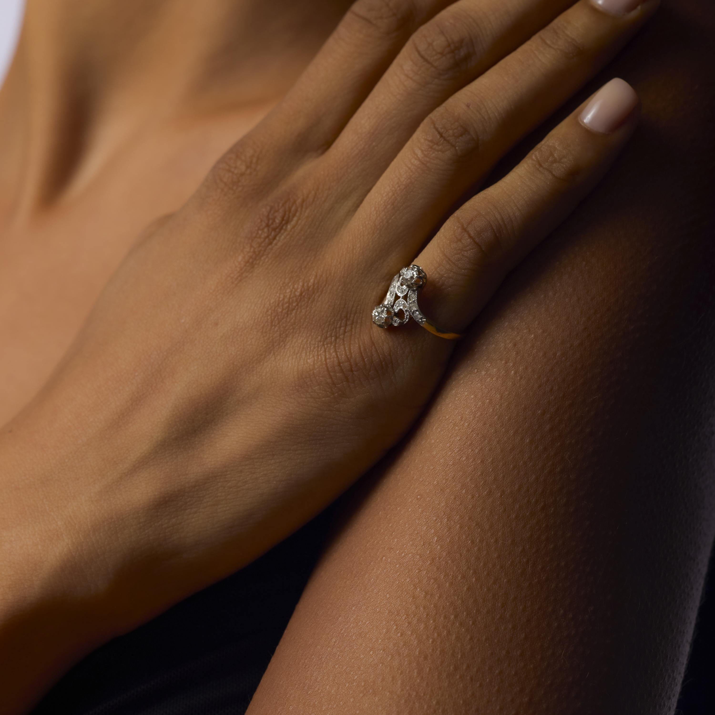 Cette bague Belle Époque associe deux diamants scintillants de taille européenne ancienne à des tailles roses dans une monture en or jaune 18 carats et en platine, évoquant un charme antique intemporel.