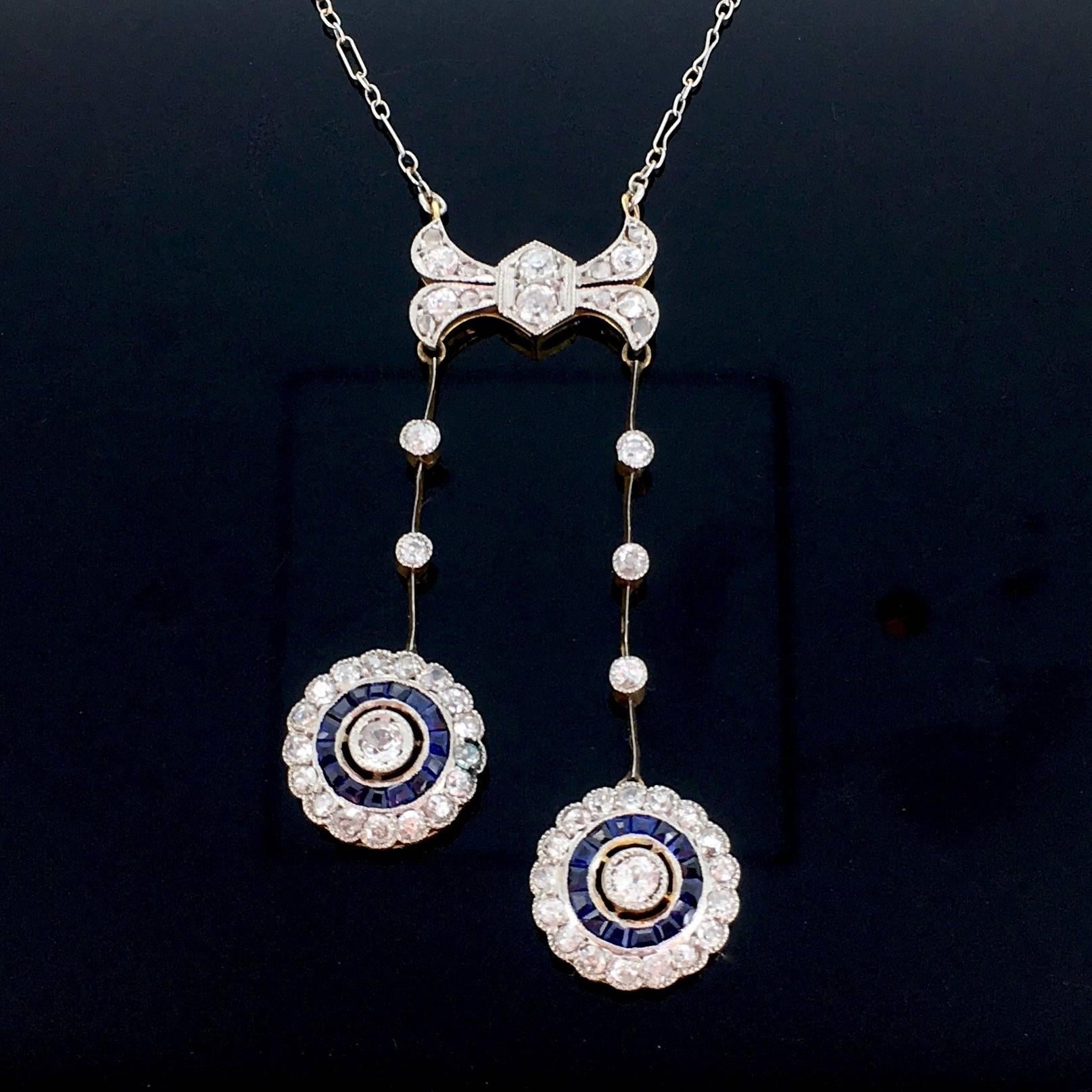 This beautiful Neglige necklace features 2 round drops set with old mine cut diamonds, surrounded with tapered cut naturals sapphires and then again with diamonds. The platinum chain is retaining on the front a knot shaped motif set with old mine