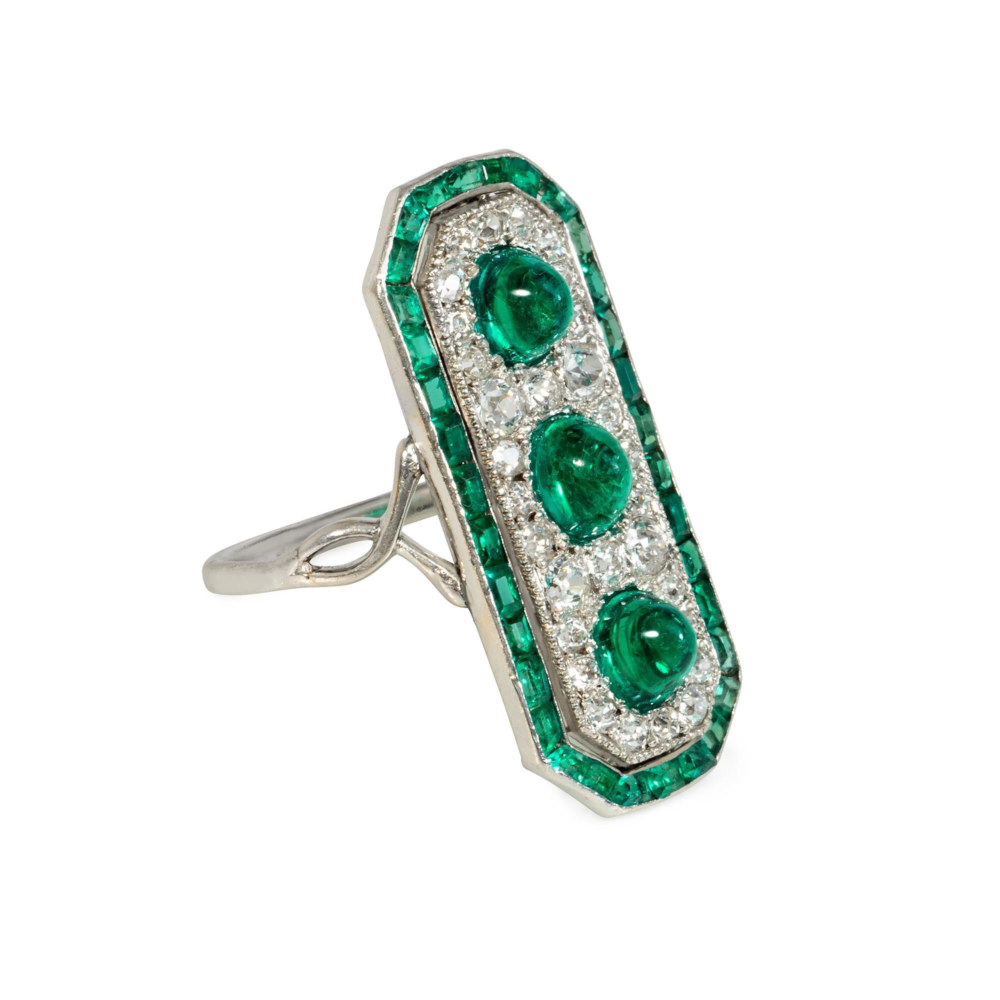 A Belle Epoque emerald and diamond rectangular plaque ring with chamfered corners, centered by three cabochon-cut emeralds surrounded by pavé old European-cut diamonds with a calibré-cut emerald border, in platinum with open twist shoulders. 