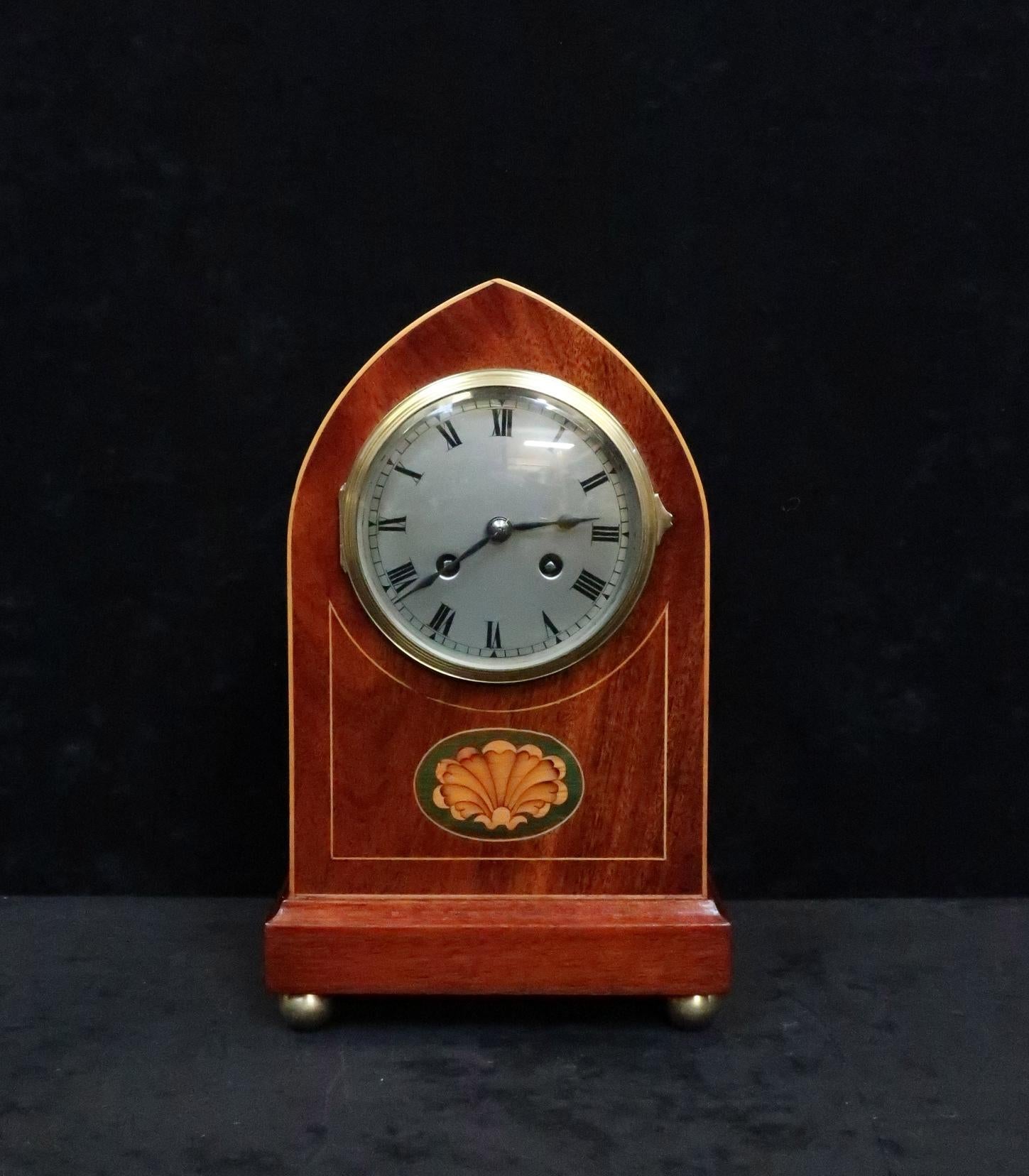 A good quality French Belle Époque figured mahogany lancet top mantel clock with boxwood stringing and shell inlay to the front of the case stood on brass ball feet. The clock has a silvered dial with Roman numerals and a French eight day movement
