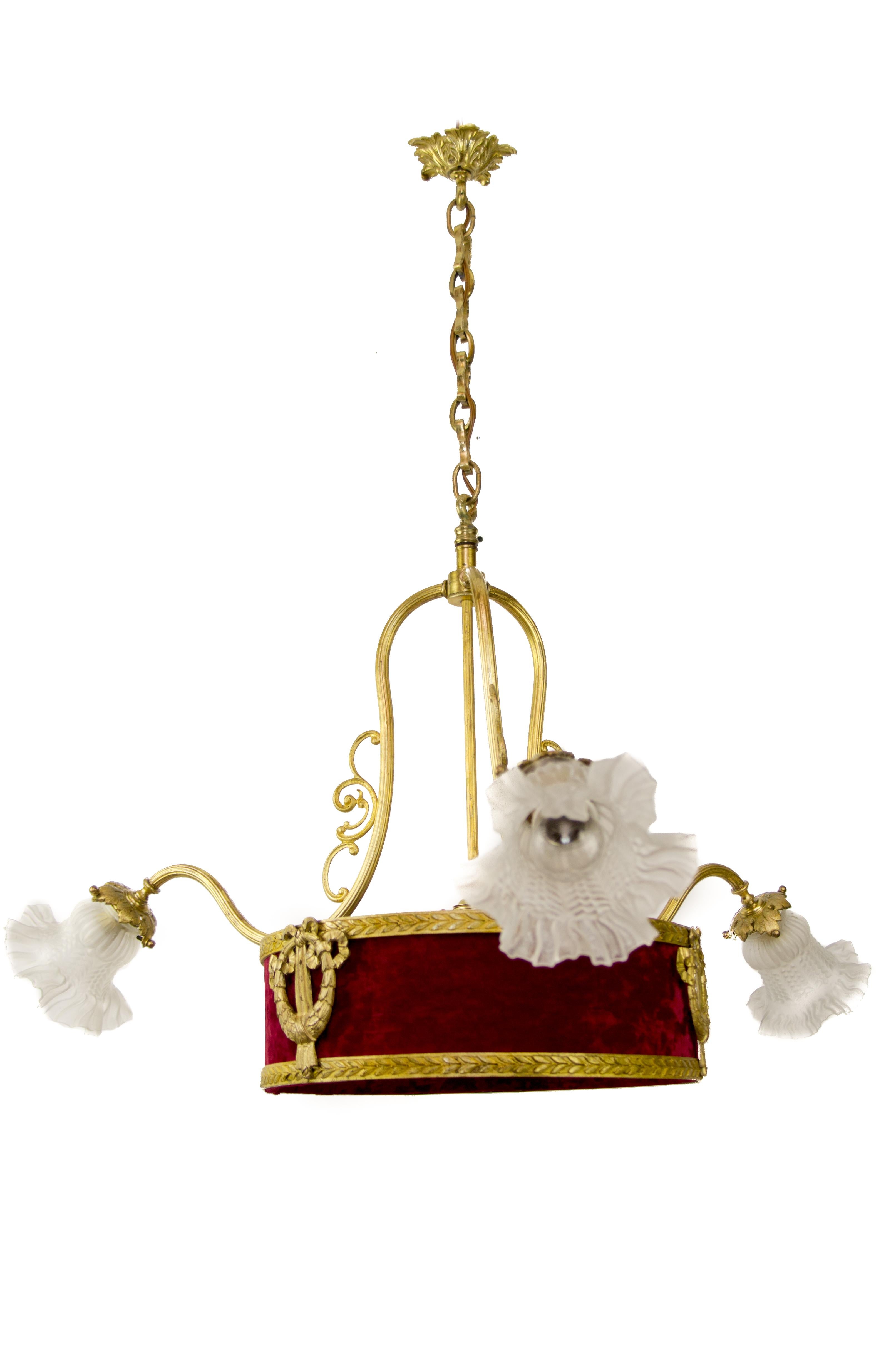 Early 20th-century French chandelier with three bronze arms, each with frosted glass lamp shade and E27 (E26) size light bulb socket. The center frame is surmounted with a red fabric shade, decorated with bronze imperial ornaments, and encloses one