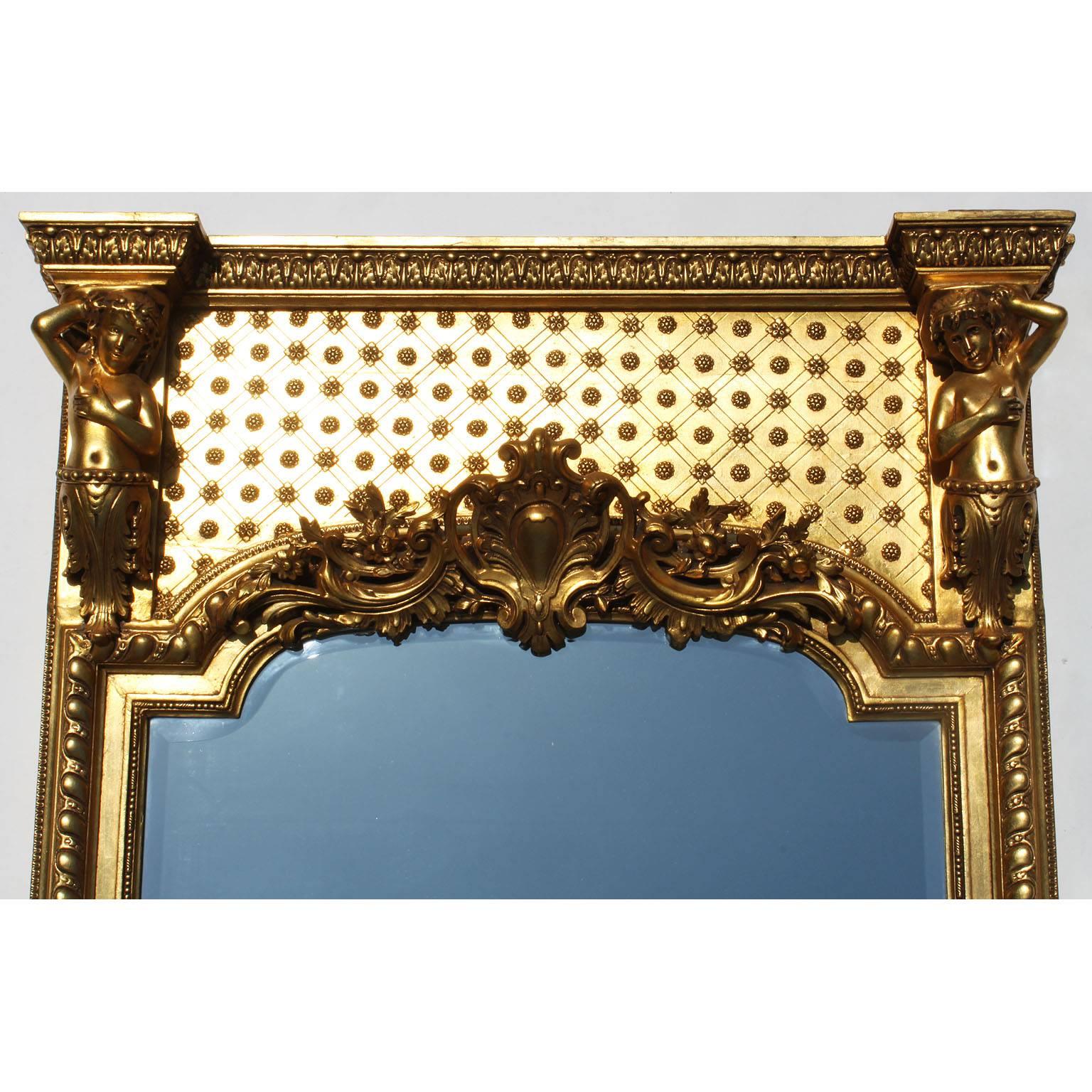 Miroir à trumeau en bois doré et sculpté à la gesso de la Belle Époque. Le cadre allongé est surmonté de chaque côté d'un Putto allégorique et centré d'un bouclier floral avec des branches d'acanthe enroulées, la plaque de miroir est biseautée,