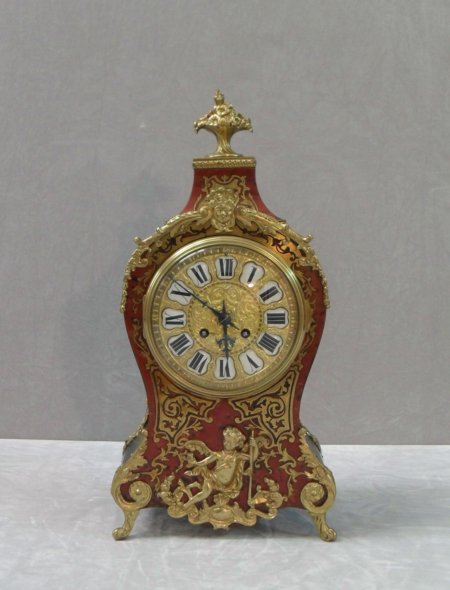 A very good quality French Louis XV style boulle red tortoiseshell and brass inlaid mantel clock with ebonized sides. The clock has decorative foliate bronze gilt ormolu mounts and moulds with cherub mount to the front, finished with floral urn to