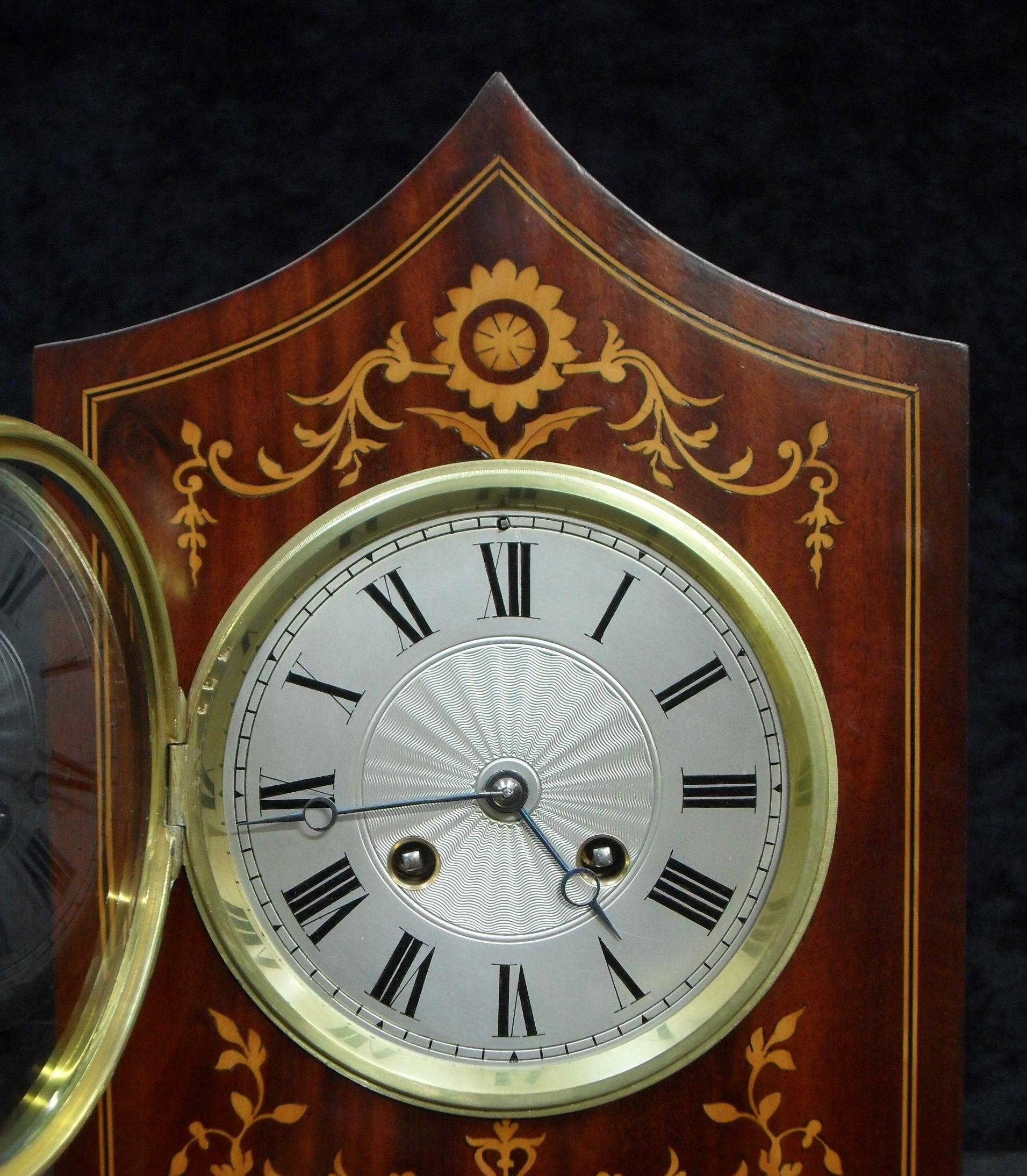 A decorative French Belle Epoque figured mahogany mantel clock with delicate boxwood inlay to the front of the case stood on brass ball feet. The clock has a silvered dial with engine turned centre and a French eight day movement which strikes the