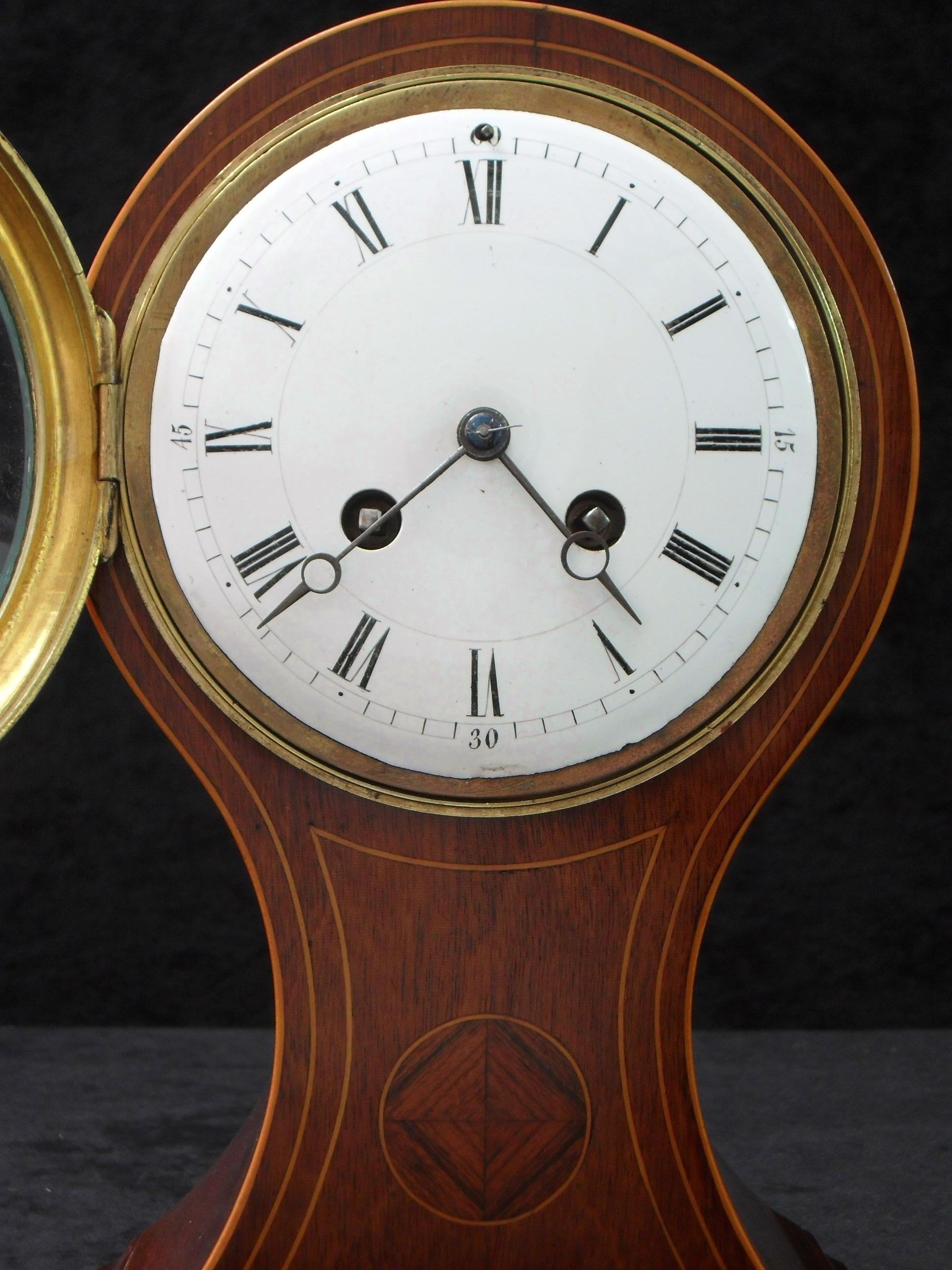 A good quality French Belle Époque mahogany balloon shaped mantel clock with inlay and boxwood string inlay to the front of the case stood on brass bun feet. The clock has a white enamel dial with an eight day French movement which strikes the hours