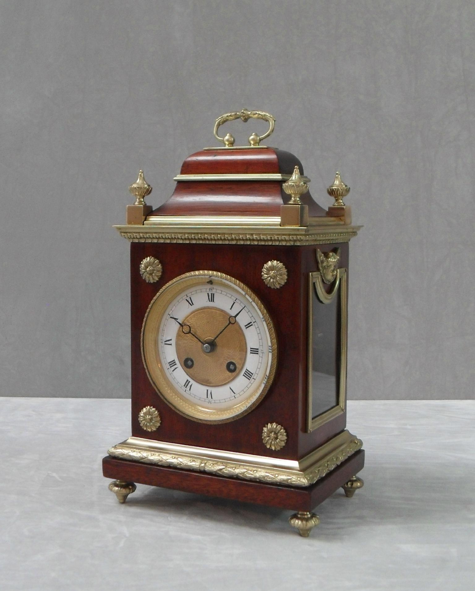 An extremely good quality French Belle Epoque mahogany mantel clock with side viewing windows, decorative bronze gilt ormolu mounts and moulds finished with four finials to the top and carrying handle. The clock dial has an engine turned centre with
