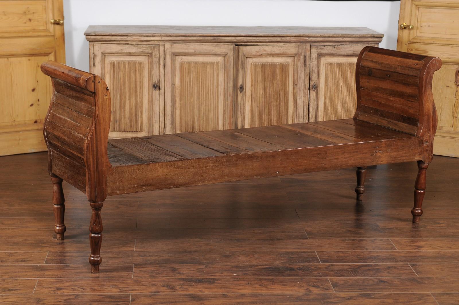 A French oak long backless bench from the early 20th century, with out-scrolling arms and turned legs. Born in France during the Belle Époque era, this elegant bench features a long rectangular seat, made of a succession of slats, flanked by two