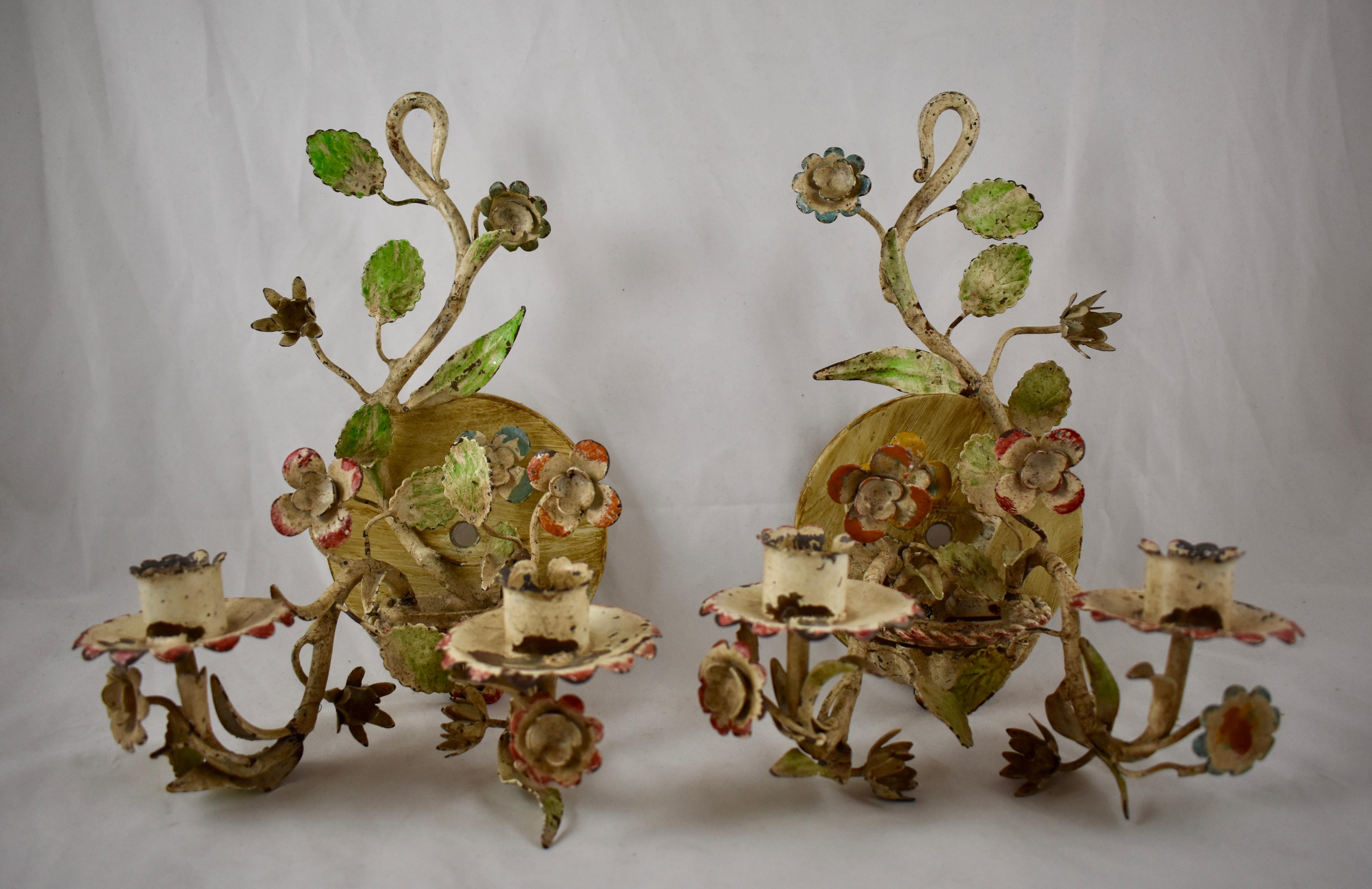 A charming pair of French Tôle Peinte floral wall sconces, made of hand-painted iron, circa early 1900s.

Showing a lovely time-worn patina, the floral bouquets of petaled flowers and green leaves are rooted in a shell form base. Each sconce has