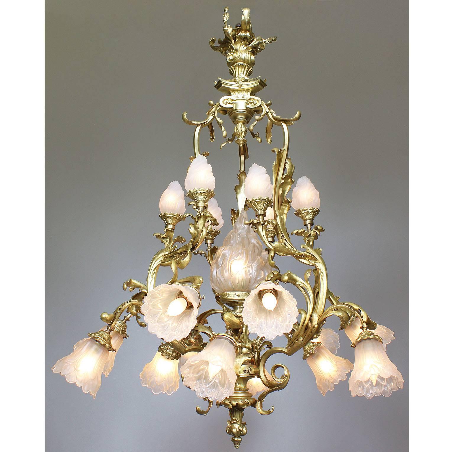 A fine French Belle Époque Rococo style gilt bronze and frosted glass shades nineteen light chandelier. The ornate gilt bronze frame surmounted six upper scrolled candle arms with frosted glass shades in the form of burning flames centered with a
