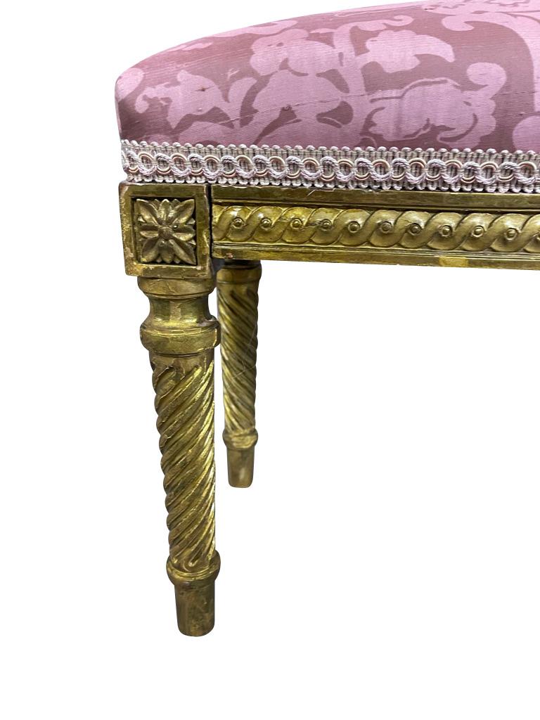 Long, low French fireplace bench with gilded legs and pink Fortuny silk. Newly reupholstered and touched up. This fireplace bench has twisted fluted legs ending in toupie feet. Rosette decoration on the corners.