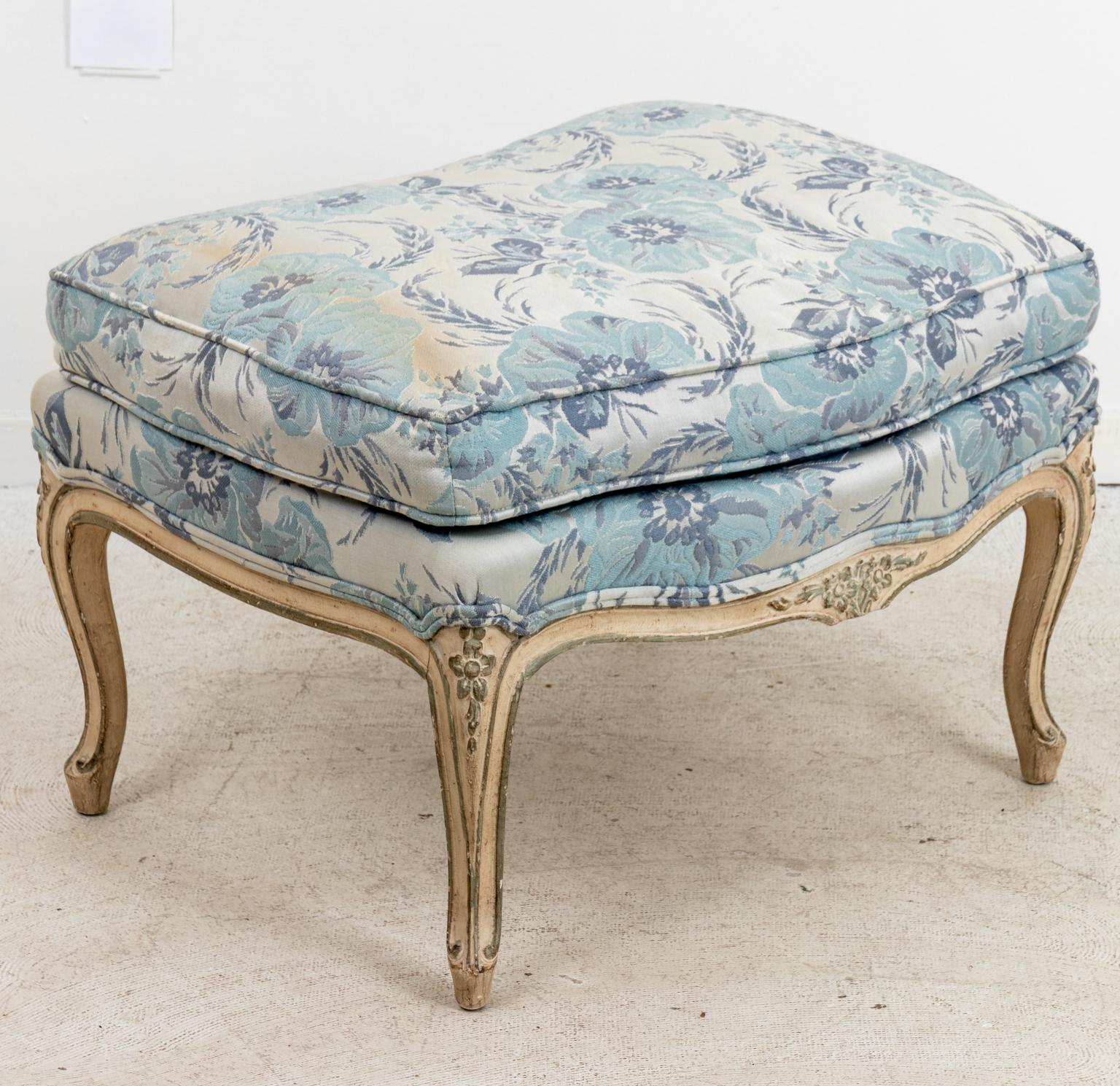 French floral upholstered bergère armchair with ottoman on cabriole legs. The pieces are detailed with carved floral motifs throughout the wood frame and upholstered armrests with scrolled detail. Please note of wear consistent with age including