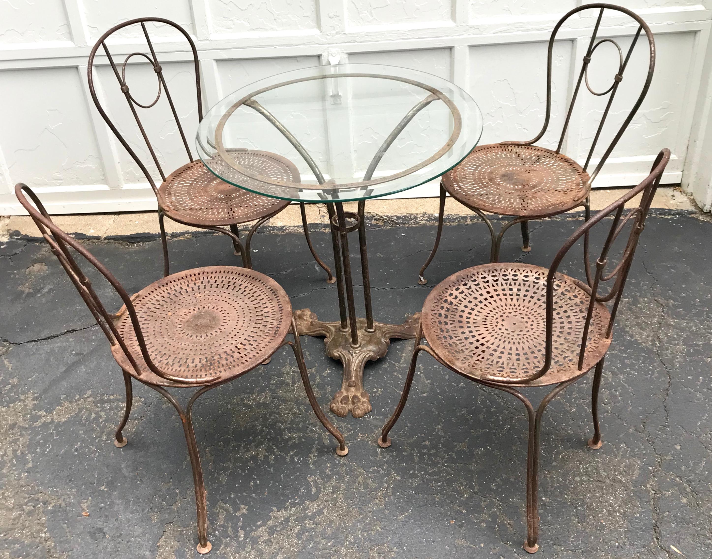 French bistro set. Set of four metal ring back chairs and round beveled glass top pedestal table perfect for breakfast nook or covered balcony/terrace French stamp “Deposé” beneath a star at center of base all on tripod claw feet. Seats of intricate