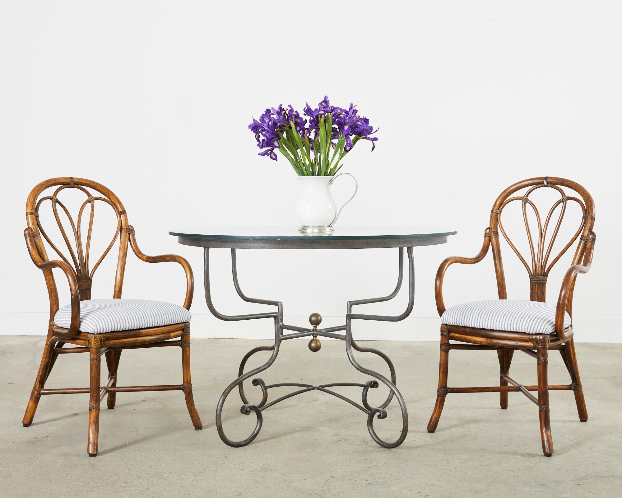 Handsome French round patio and garden dining table crafted from iron. The table features four gracefully curved scroll legs conjoined by a round stretcher and topped with a 1/2 inch thick round pane of glass. The legs are conjoined by cross