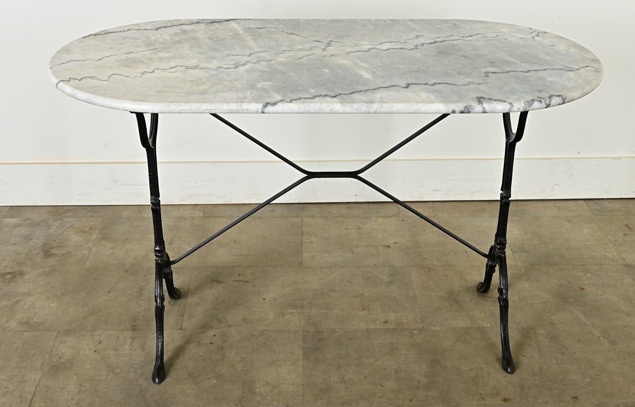 A classic French bistro table with oblong, gray marble top on black, cast iron base. The natural stone has a smooth, honed finish over the expressive vein patterns and is rounded on the edges. Discoloration and etching of the marble is consistent