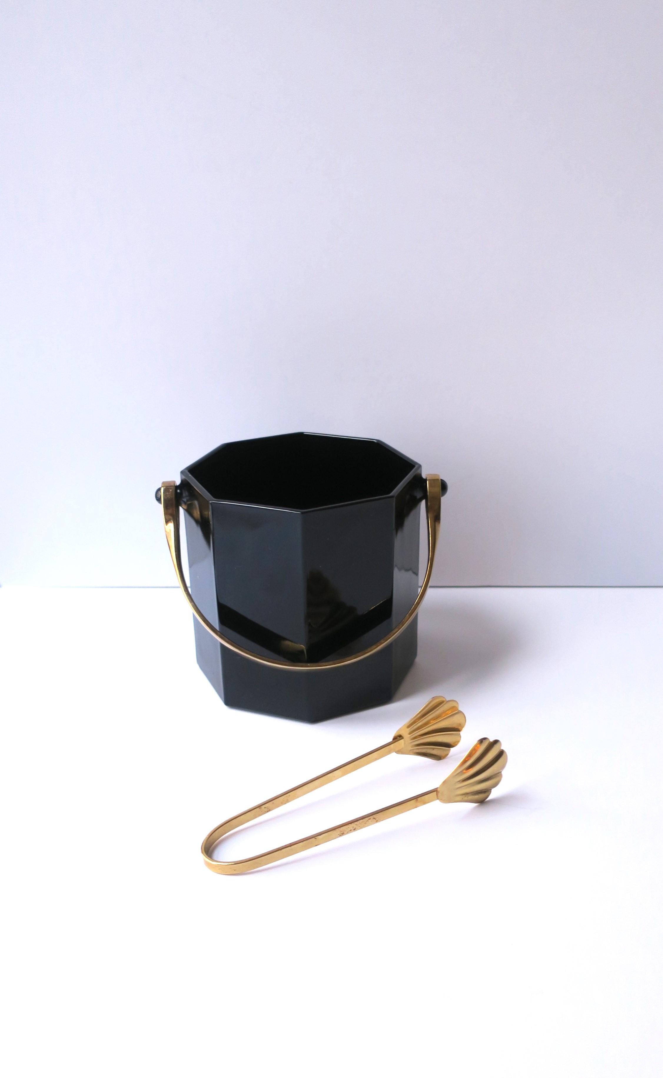 A chic French black glass ice bucket with ice tongs, of the '70s Modern period, circa 1970s, France. Bucket is black glass in an octagonal shape with a gold-tone handle. The octagonal shape bucket is a nice alternative to round. The tongs are a