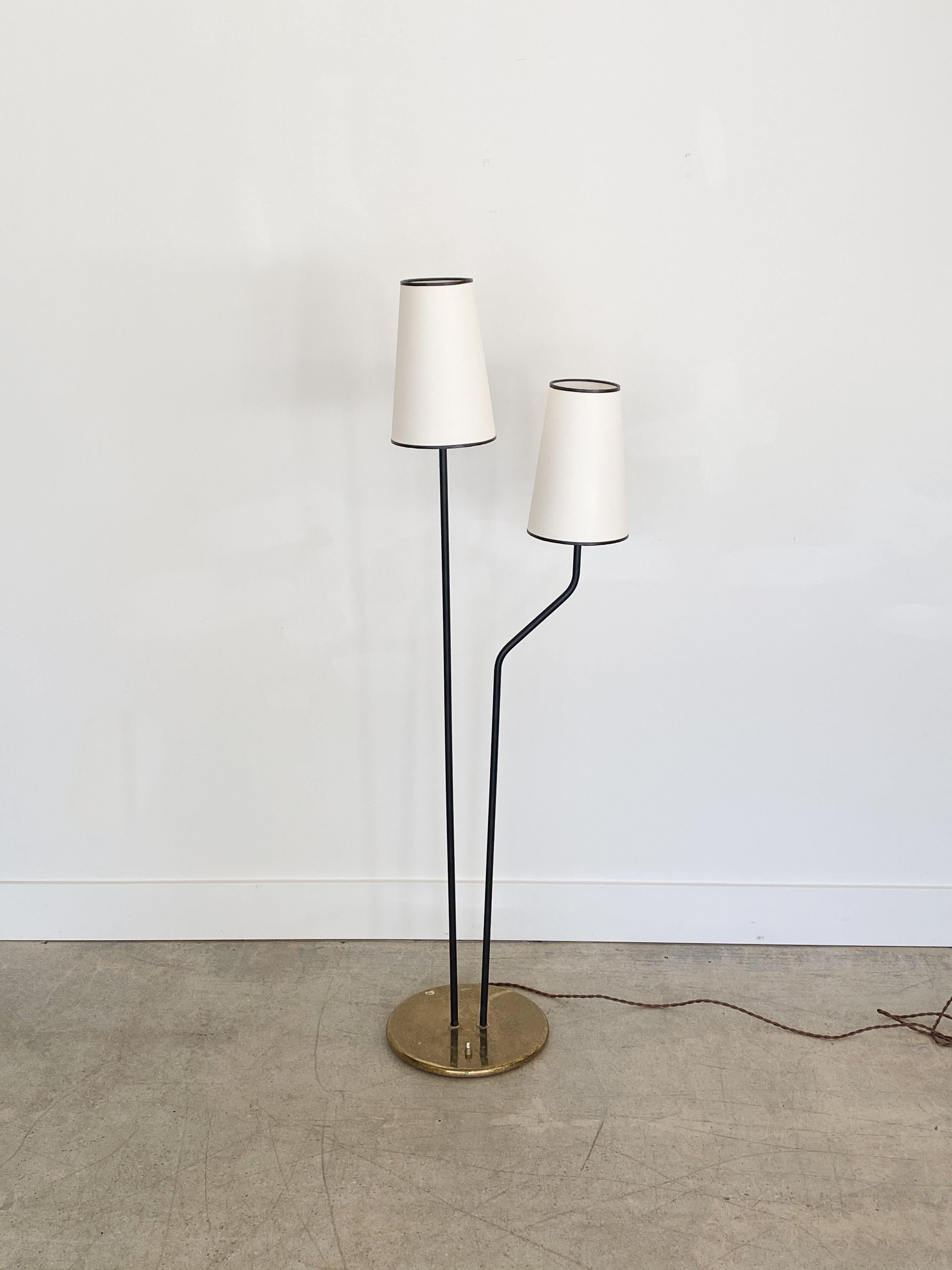 Black iron two-light floor lamp from France, 1950s. Circular brass base with two black painted iron stems each with a single socket. Newly rewired and new paper shades. Original condition showing scratches, age, and patina.