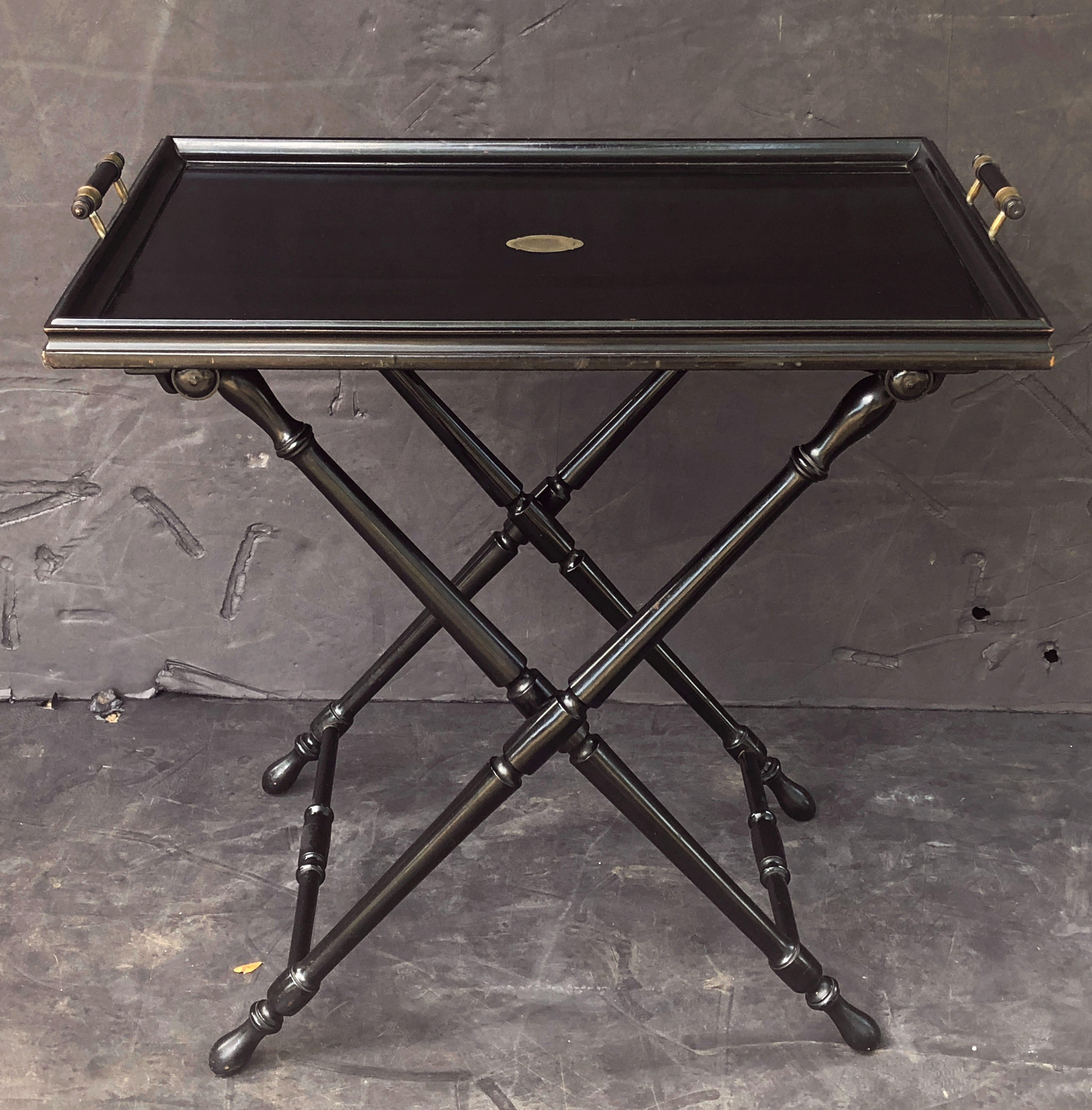 A fine French butler's tray table on stand, featuring a black lacquer or ebonized rectangular serving tray set upon a folding X-shaped stand.
The tray with a raised, moulded edge with a brass cartouche in the centre and brass and wood handles. The