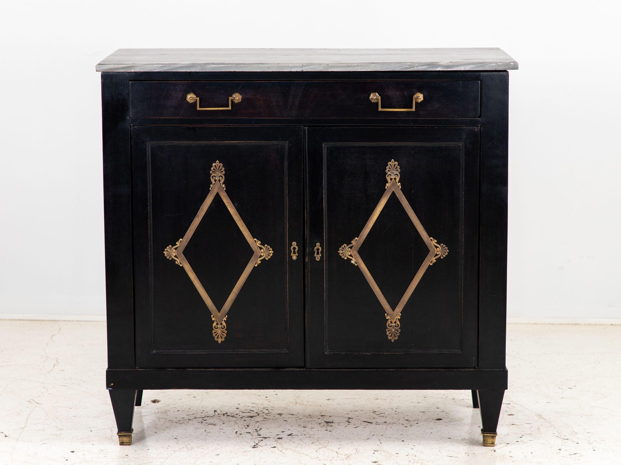 This later black-painted buffet with a luxurious marble top exudes sophistication and timeless style. Its sleek black finish adds an air of refinement to any space, while the two elegantly crafted doors are adorned with brass lozenge details that