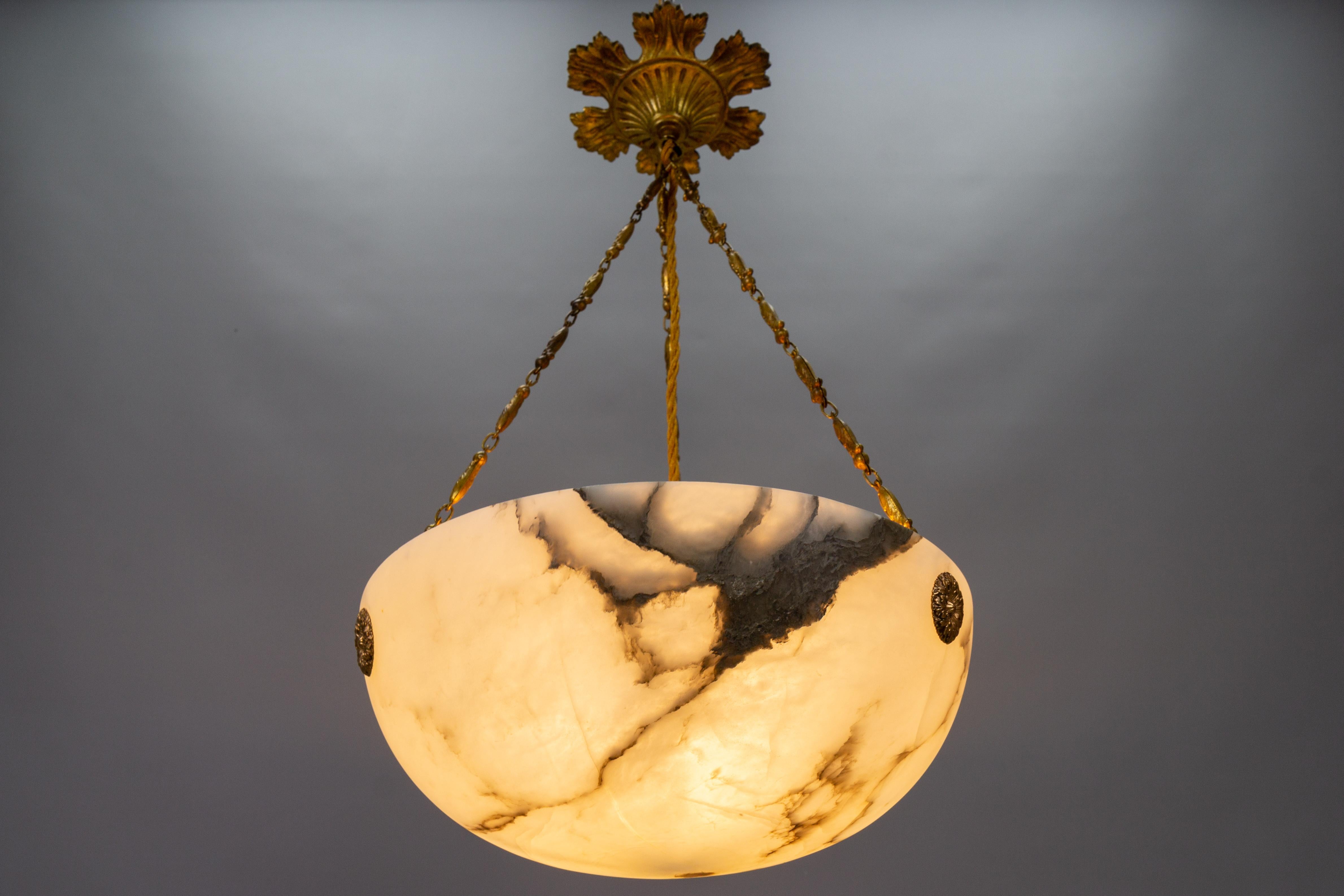 Art Nouveau soft white and black veined alabaster pendant light fixture.
An adorable alabaster pendant ceiling light fixture from circa the 1920s. Beautifully veined and masterfully carved soft white alabaster bowl suspended by three decorative