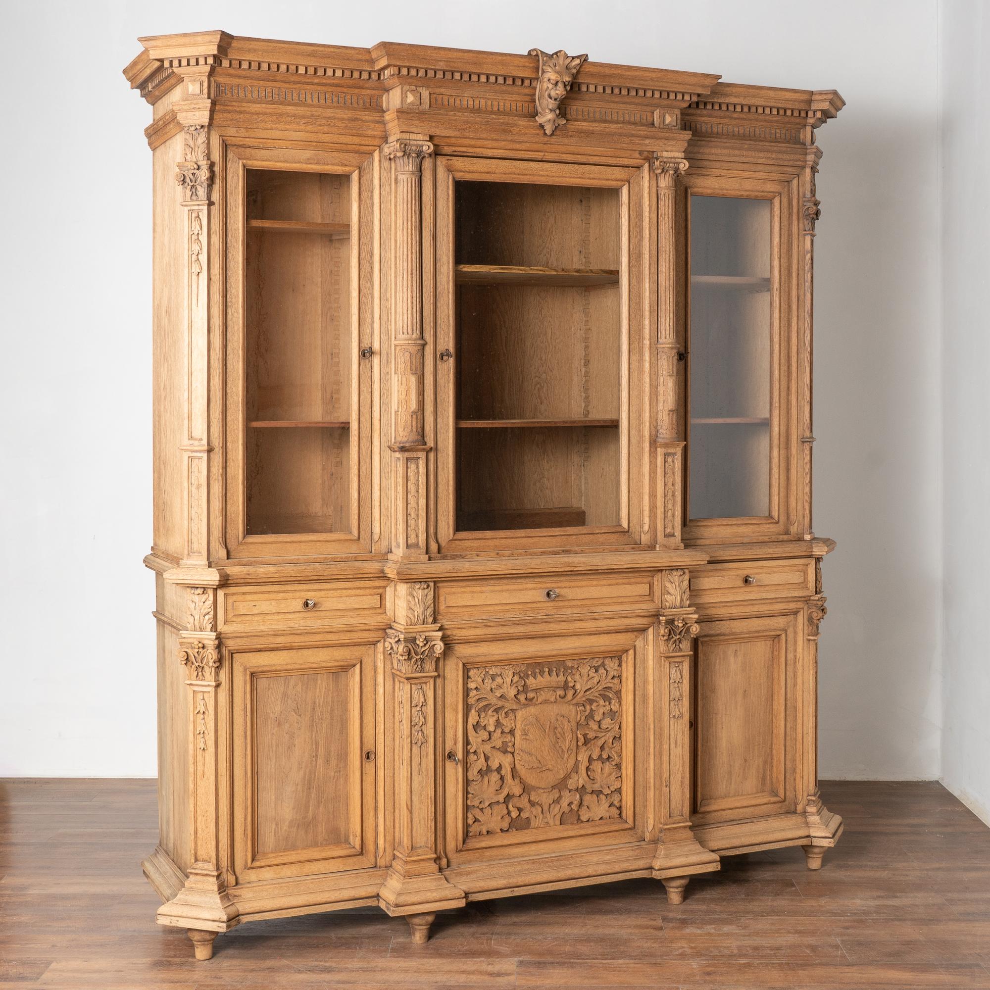 Questa grande libreria in rovere sbiancato è di dimensioni statuarie ed è caratterizzata da uno stemma di famiglia intagliato con corona, dettagli a mezza colonna e altro ancora.
Con un'altezza di 8', le 3 ante in vetro aumentano l'impatto visivo di