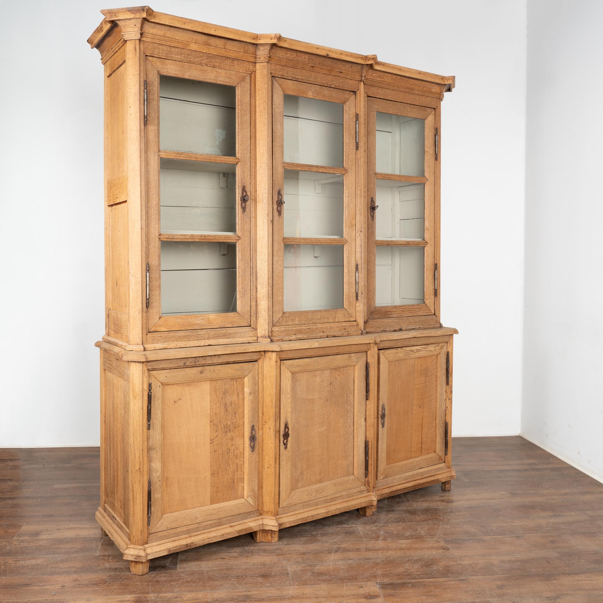 This large bleached oak bookcase is statuesque in size. At over 7' tall, the glass door panes add to its visual impact displaying any collection held within.
This cabinet is built in 2 sections, making it easier to install the heavy oak lower