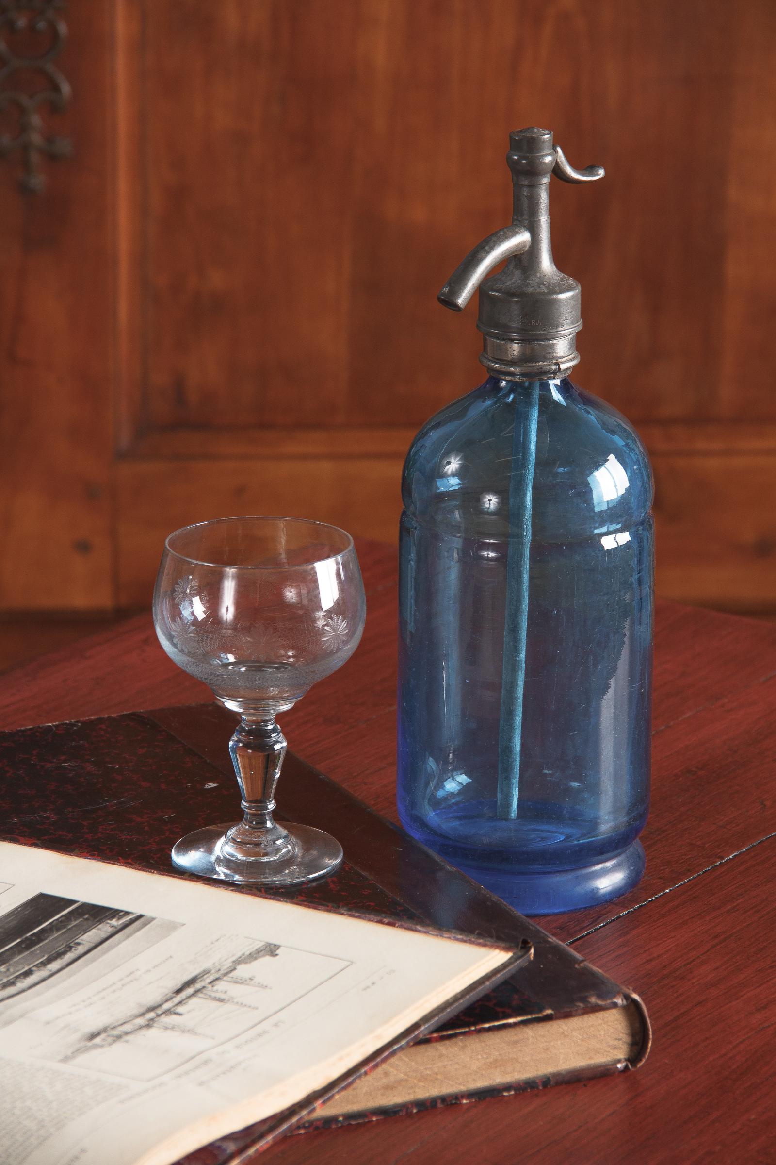 A decorative blue glass seltzer bottle from France. Thick, light blue glass bottle with subtle molding and an old metal siphon, possibly pewter. Partially worn markings on the siphon indicate a Parisian street address. Great decor piece.