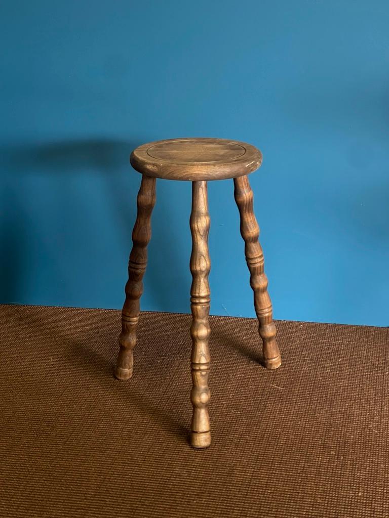 Frappant et sculptural, ce tabouret en bois massif des années 1960 illustre l'élégance brute du brutalisme français. L'épaisse assise circulaire, sculptée dans un seul bloc de bois, est soutenue par trois pieds robustes aux détails dramatiques