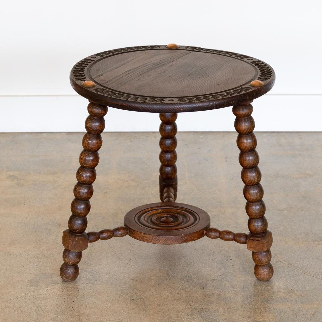 Beautiful bobbin wood tripod table from France, 1940s. Circular wood top with carved floral design around edge and brass detail. Three bobbin leg base and ball feet. Original finish shows great age and patina. Stunning statement piece.