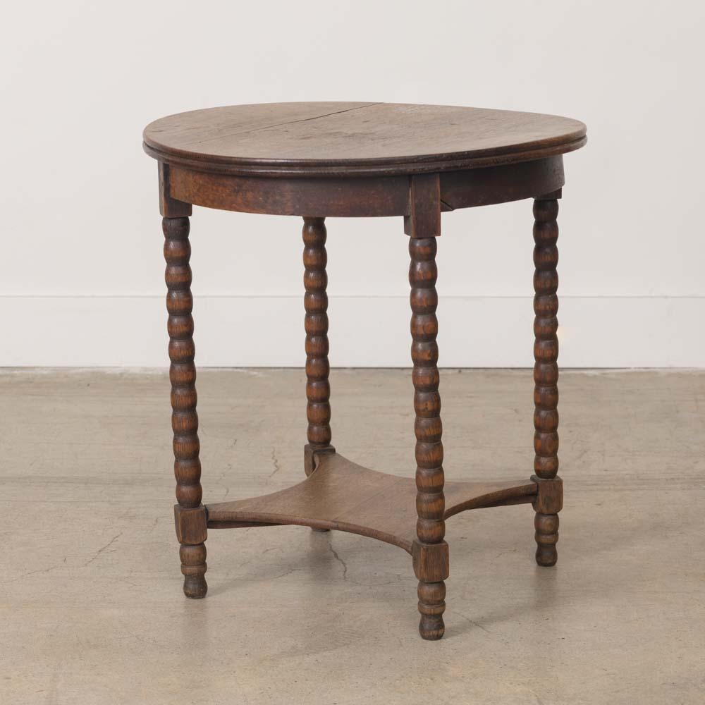 Grazioso tavolino a due piani in legno intagliato proveniente dalla Francia, anni '40. Piano circolare con ripiano inferiore e quattro gambe a rocchetto intagliate. La finitura originale mostra una buona età e patina. 