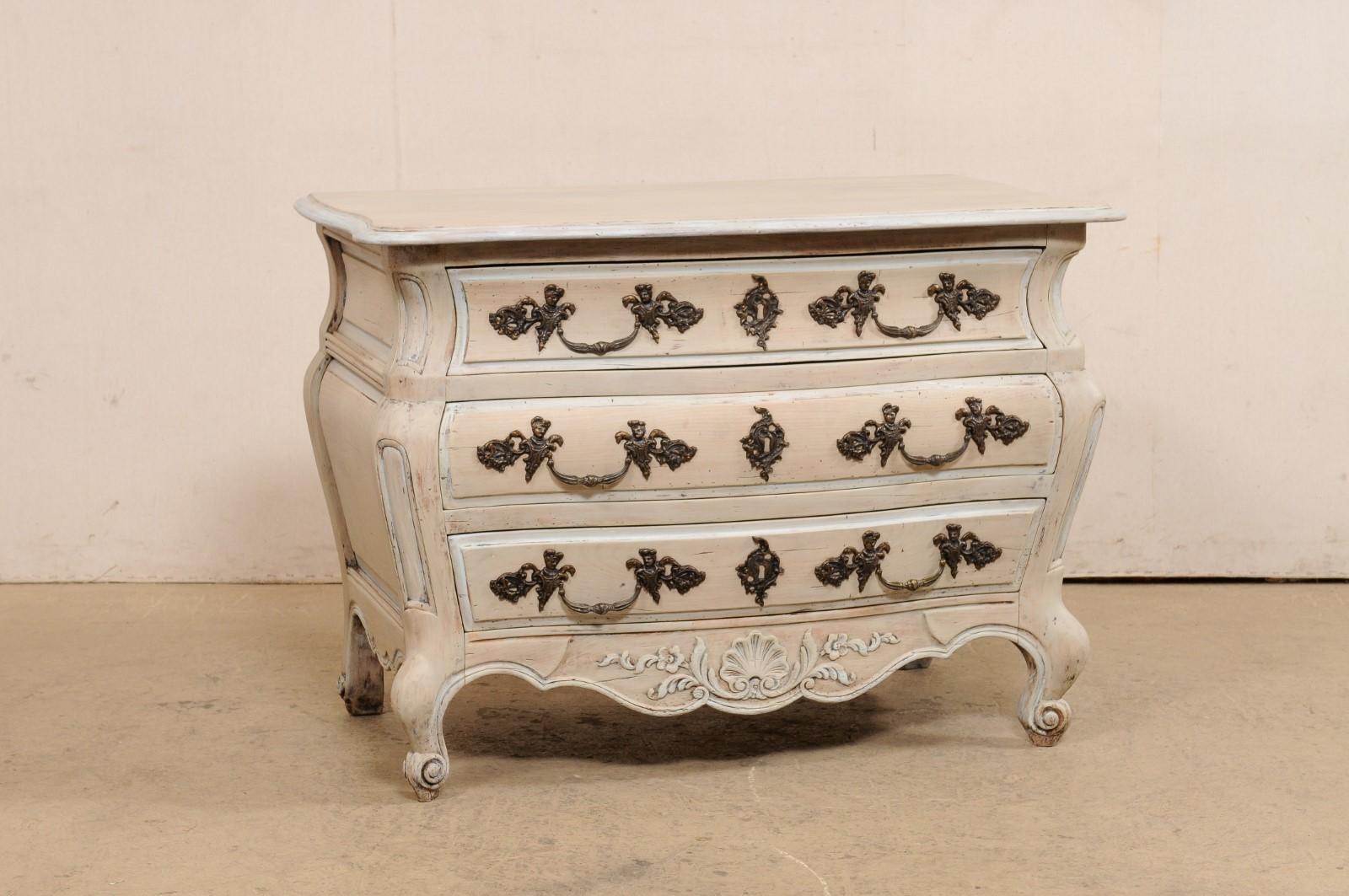 A French carved and painted-wood chest of three drawers. This vintage chest from France features a curvy bombé style case, scalloped skirt along three sides, decorative panel carvings down each front side post, and raised panel sides. The chest